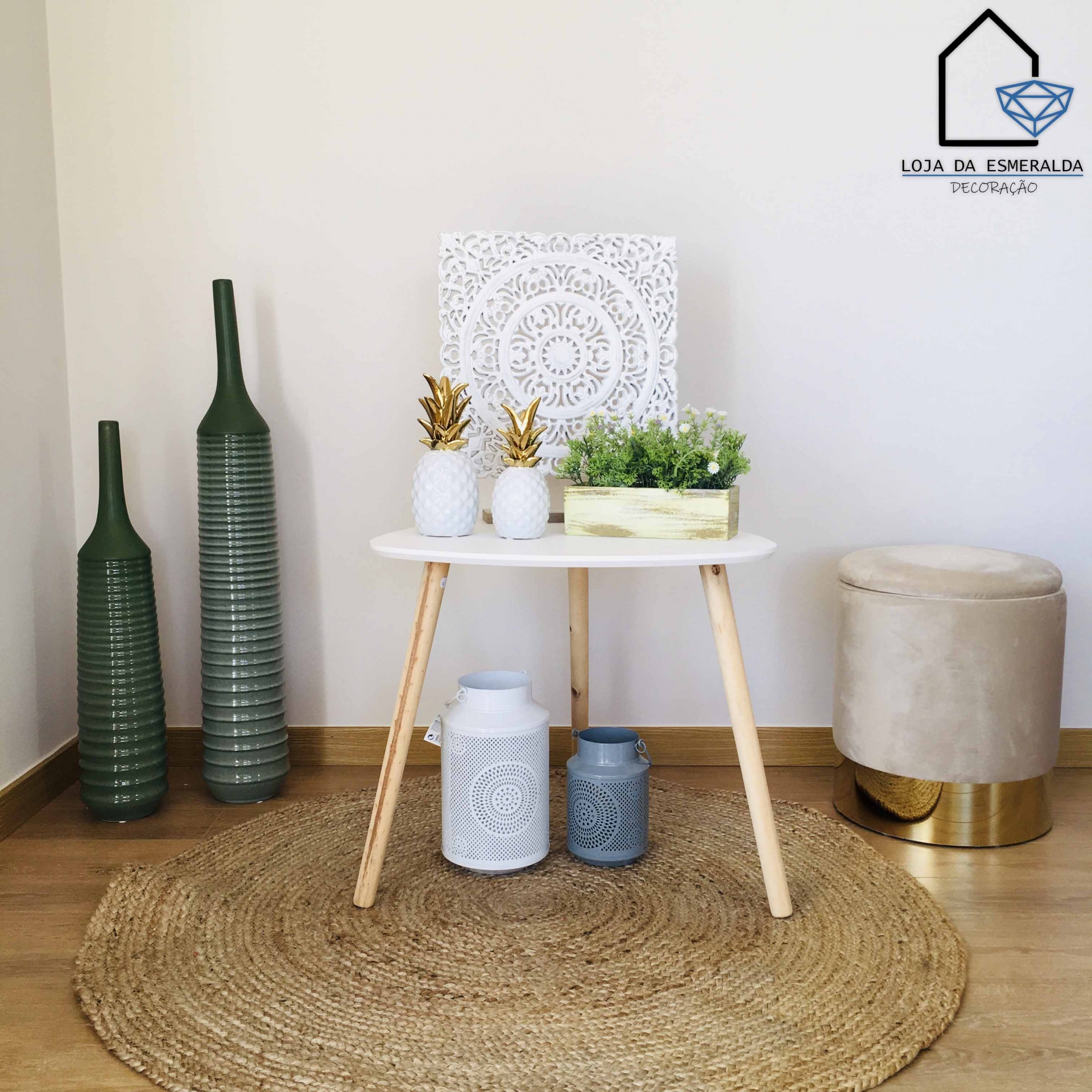 Mesa de madeira clara com tampo branco rodeada por vasos decorativos, banquinho e tapete redondo de fibras naturais