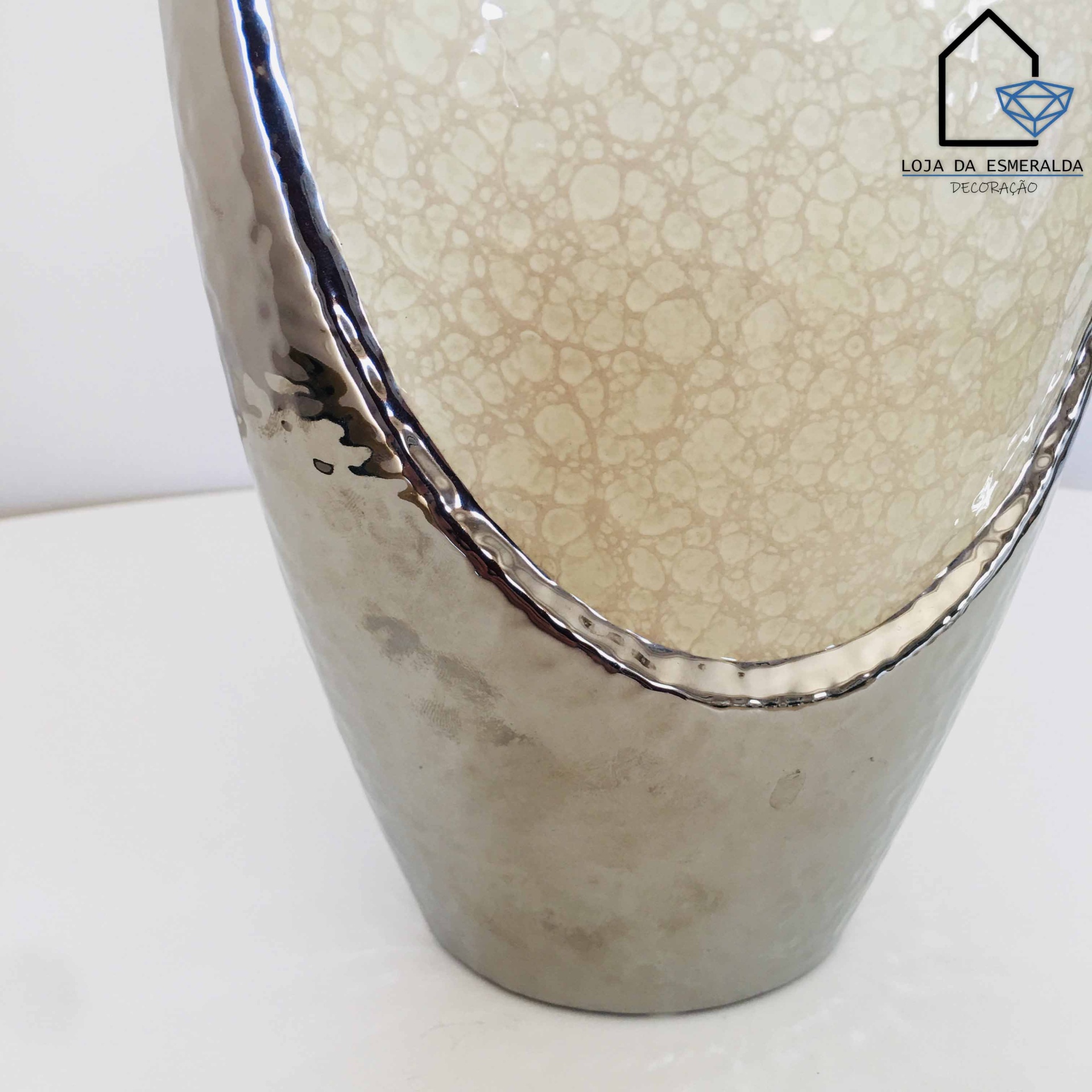 Vaso decorativo metálico prateado com interior bege craquelado sobre superfície branca