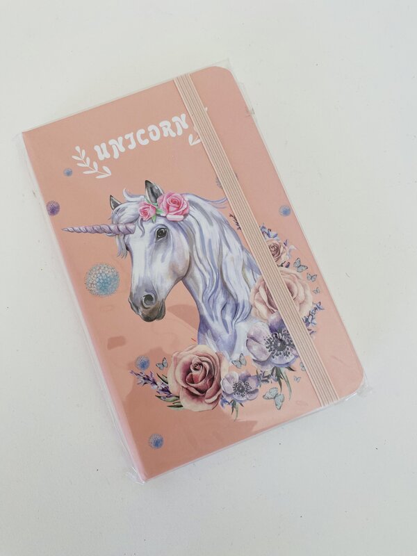 Caderno cor-de-rosa com ilustração de unicórnio e flores, texto UNICORN na capa