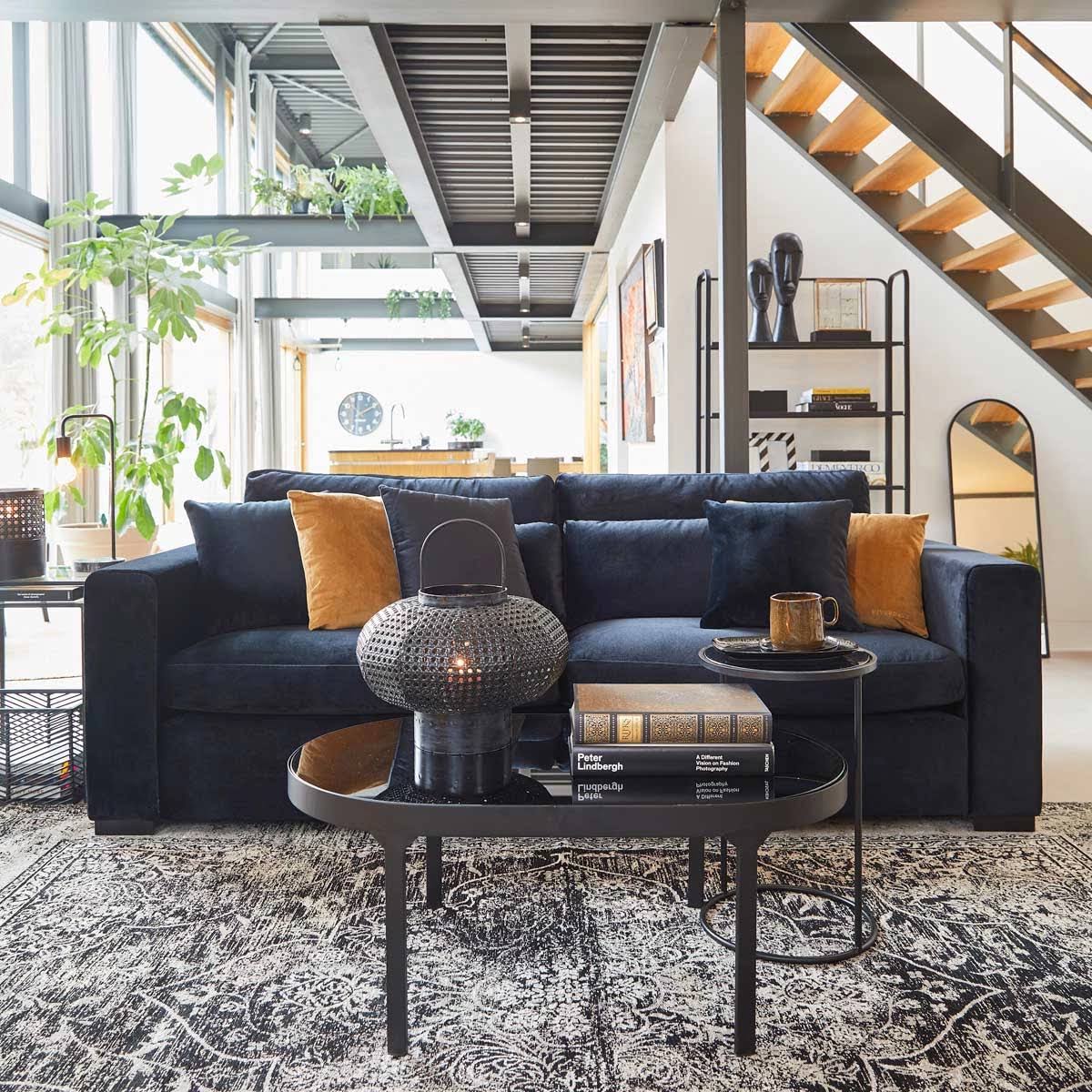 Sofá azul escuro com almofadas amarelas e azuis em sala moderna com mesas de centro e escadas de madeira
