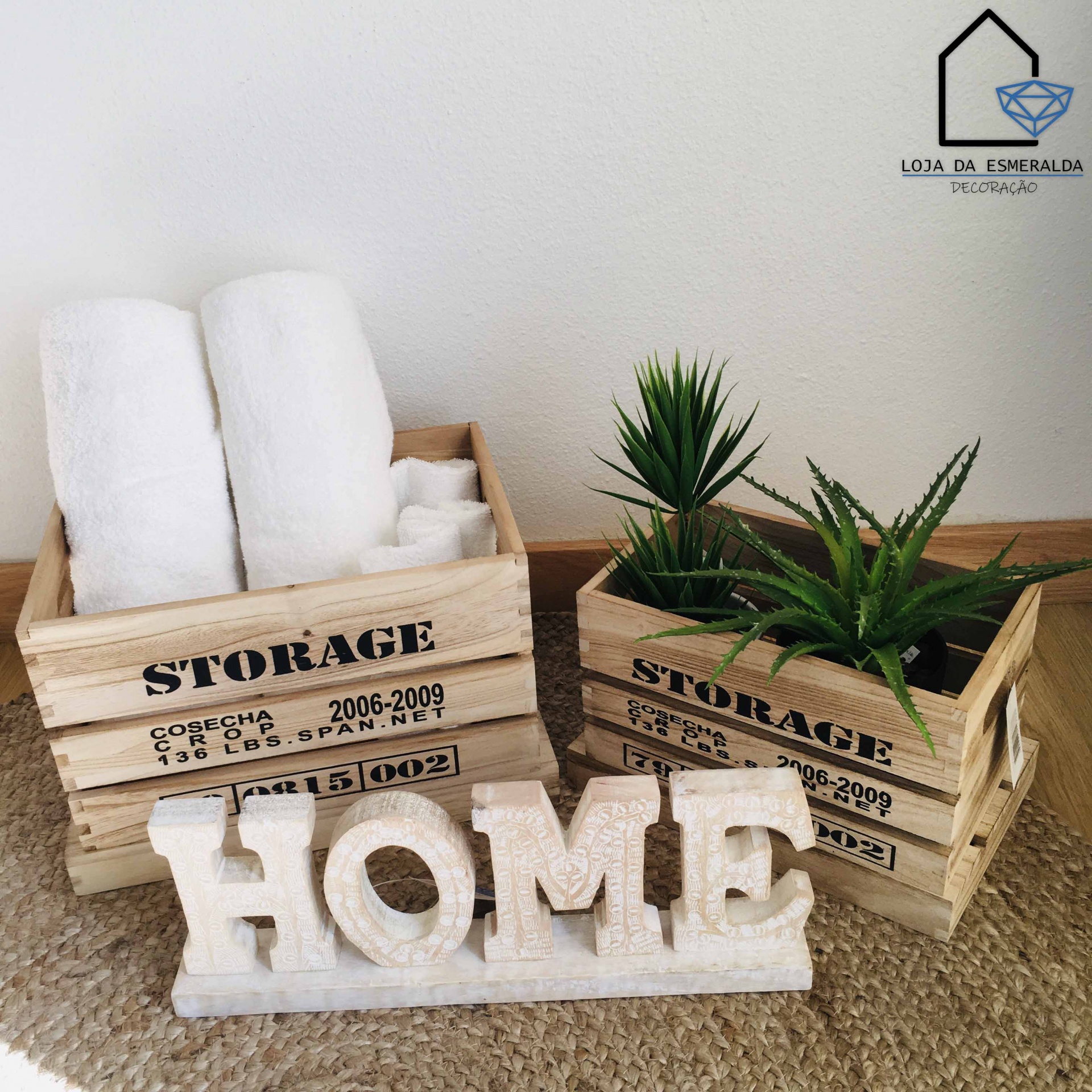 Caixotes de madeira com toalhas e plantas, palavra HOME em decoração e logotipo da loja na parede