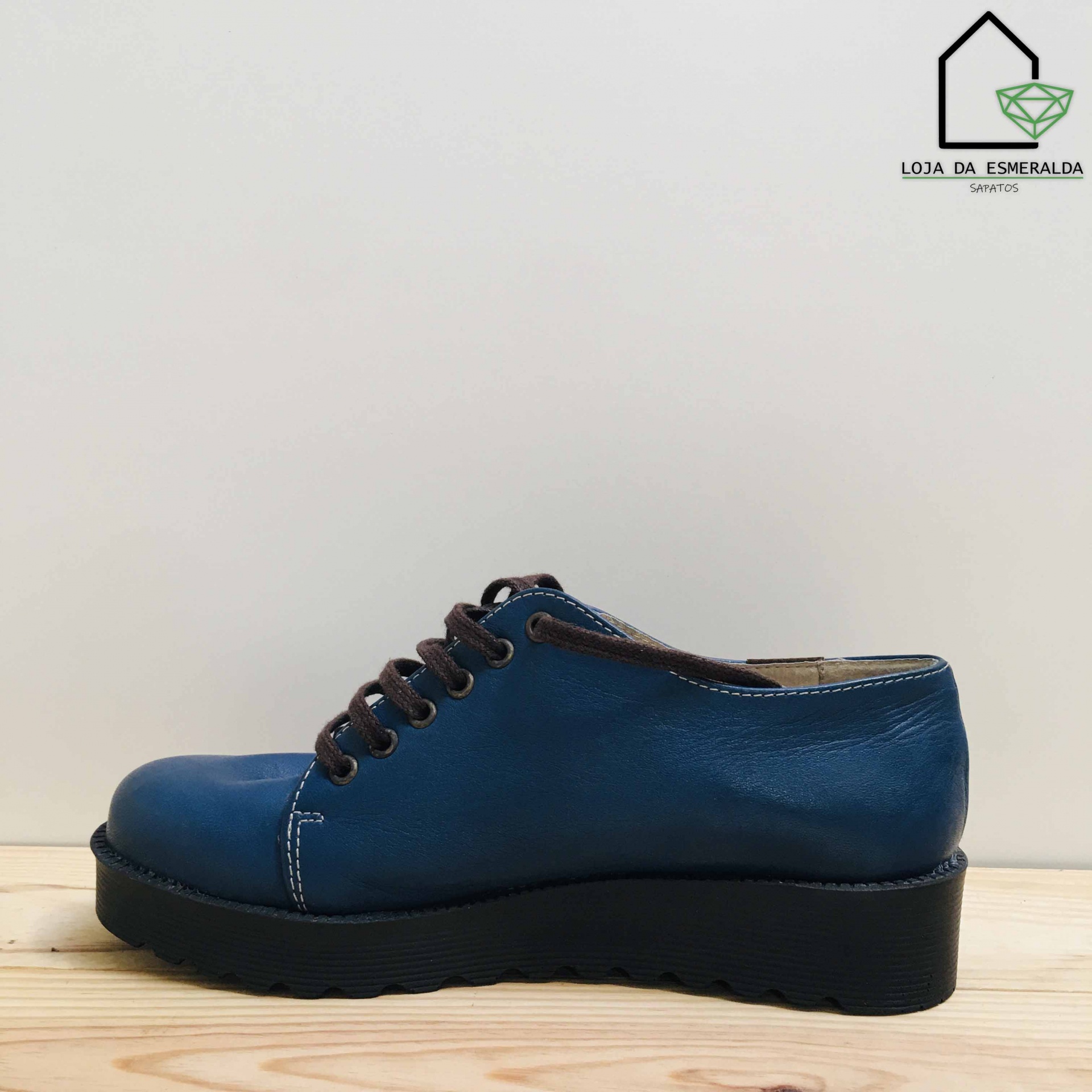 Sapato de couro azul com atacadores castanhos e sola preta em fundo branco