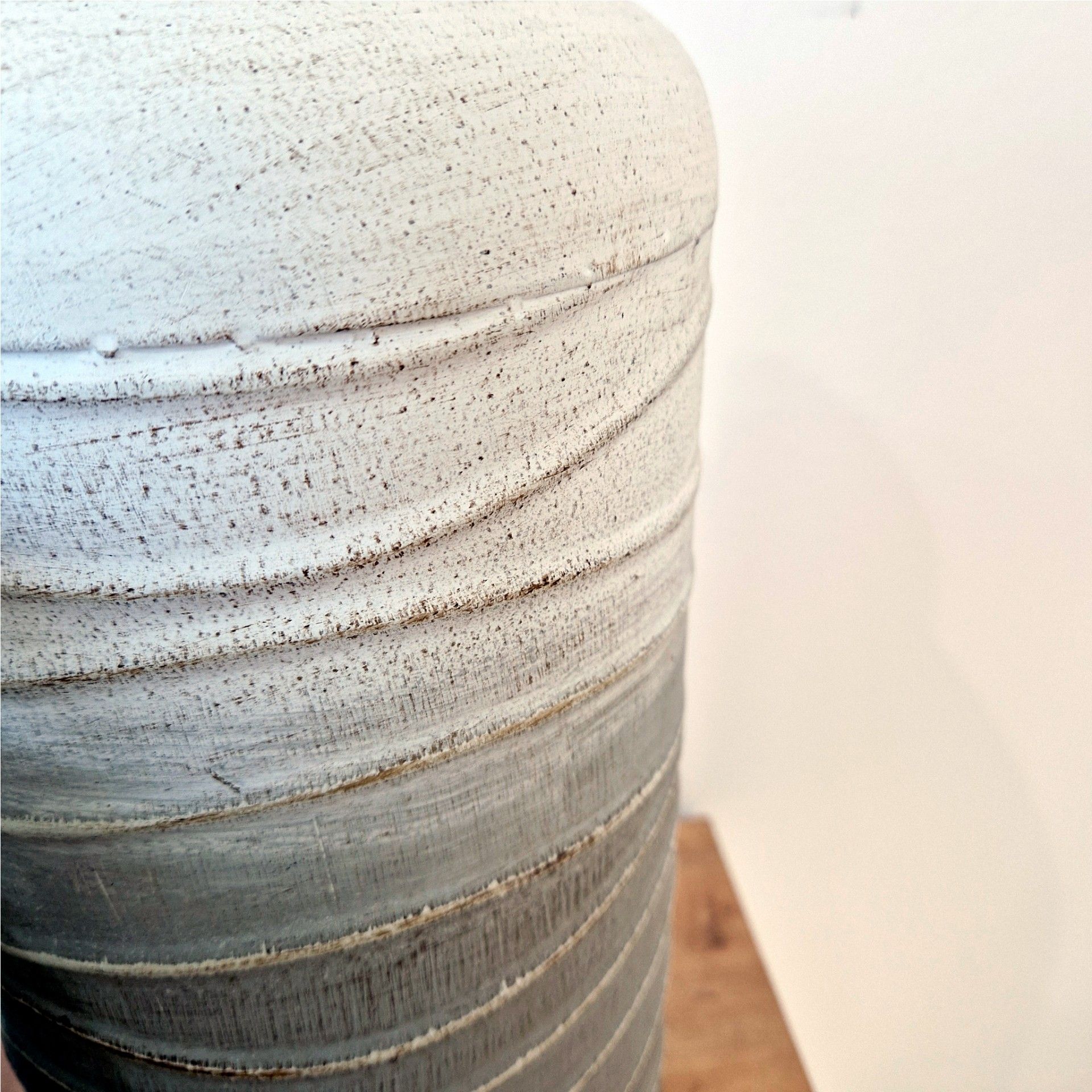 Vaso cilíndrico texturizado em cinza e branco sobre chão de madeira