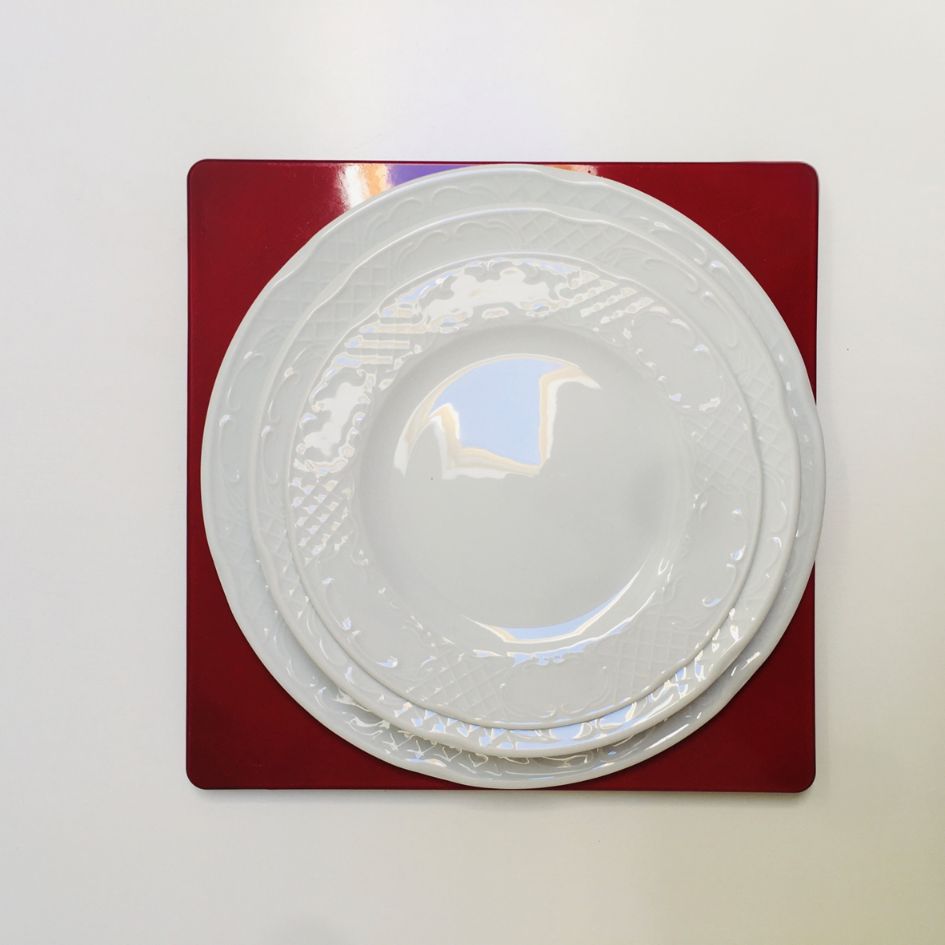 Três pratos brancos empilhados sobre jogo americano vermelho