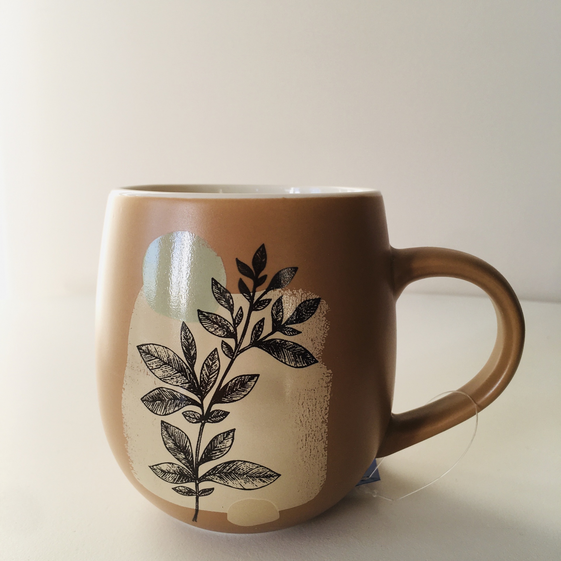 Caneca castanha com estampa de folhas pretas e verdes sobre manchas creme