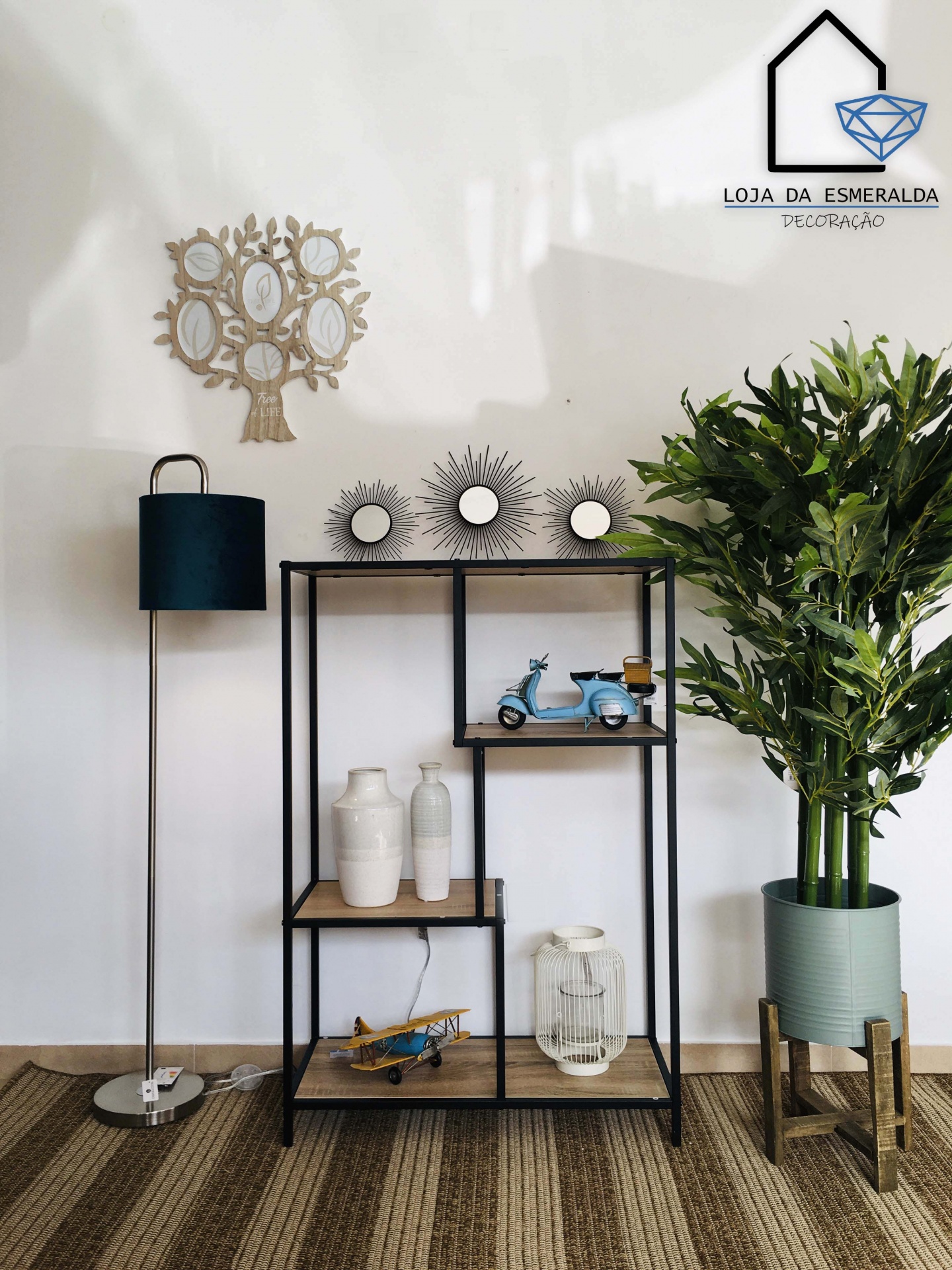 Estante decorativa preta com prateleiras de madeira clara e objetos decorativos, planta verde em vaso cinza e luminária de pé preta