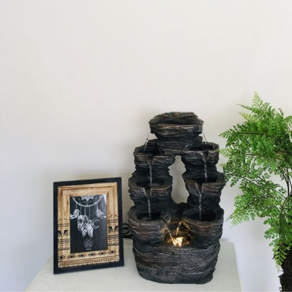 Fonte decorativa de água em resina e moldura com ilustração ao lado de planta verde