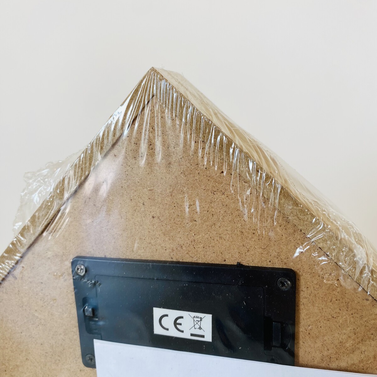 Parte traseira de estrutura triangular de madeira clara com caixa preta e símbolos CE e reciclagem