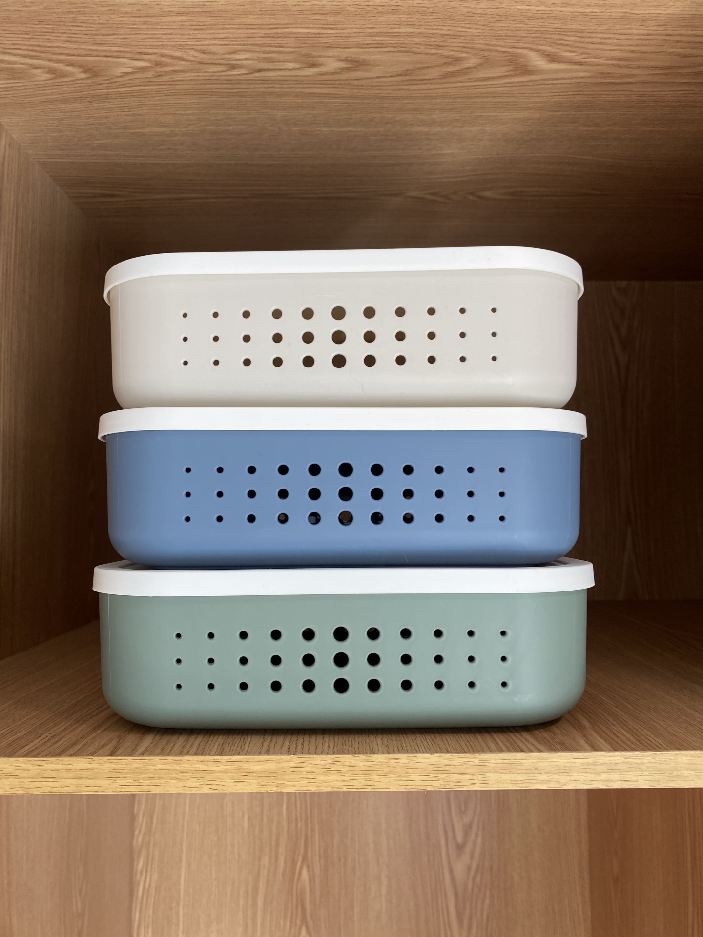 Três caixas organizadoras coloridas com tampas brancas em prateleira de madeira