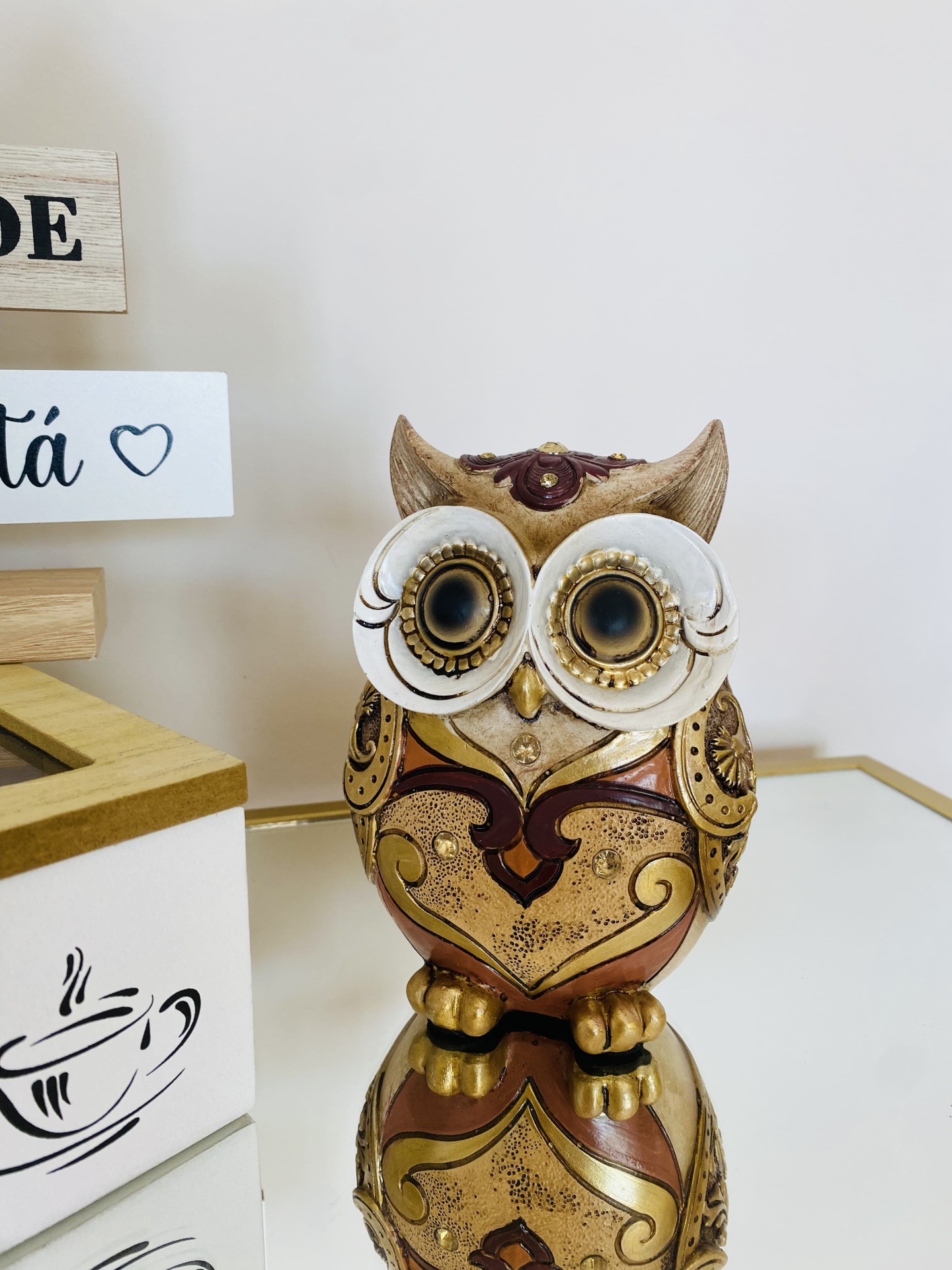 Estátua decorativa de coruja dourada e bronze com olhos grandes sobre superfície espelhada