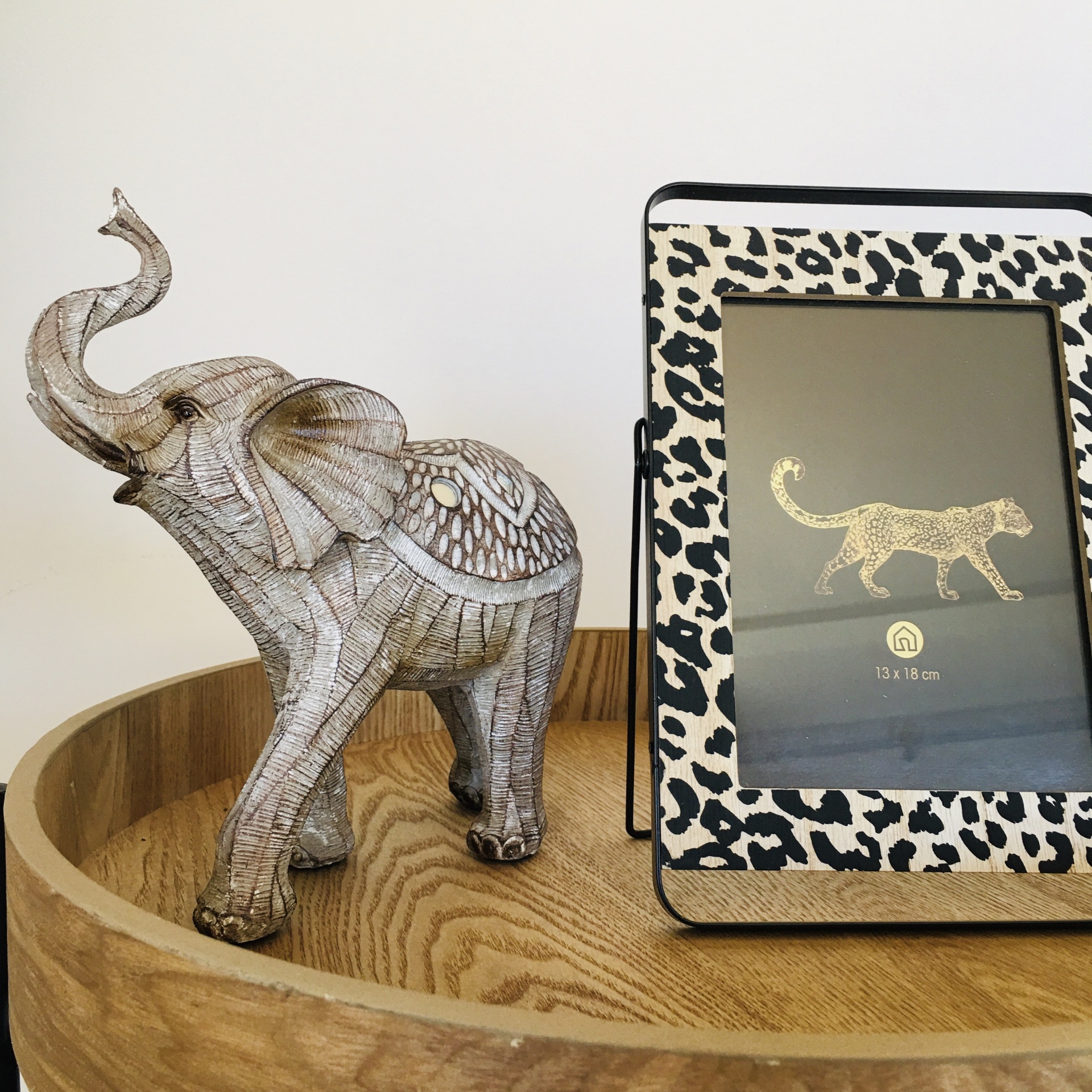 Elefante decorativo de cerâmica e porta-retratos animal print sobre bandeja de madeira.