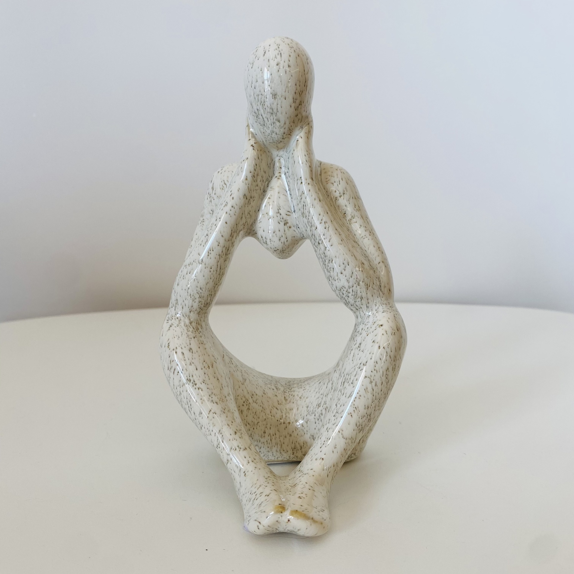 Escultura decorativa de figura humana sentada em cerâmica branca com textura cinzenta