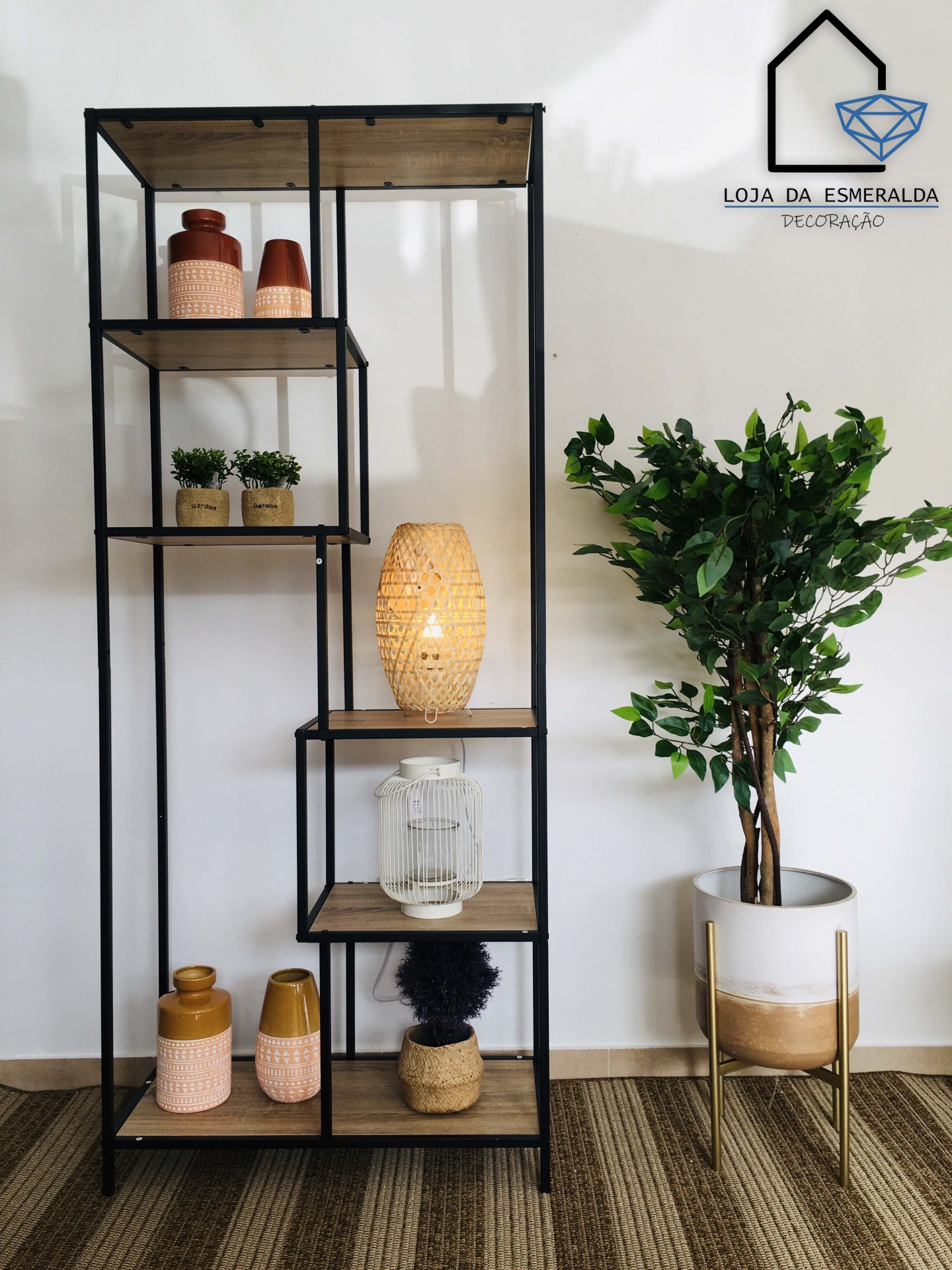 Estante metálica com prateleiras de madeira e decoração, planta artificial ao lado, parede branca com logo