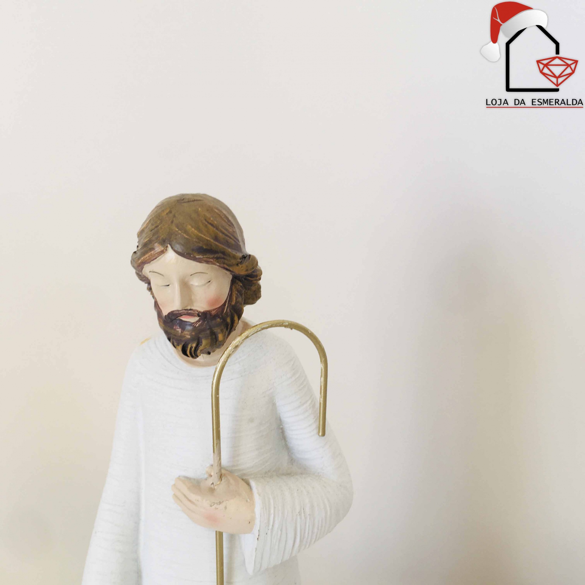 Estátua de Jesus com túnica branca e cajado dourado em fundo claro com logotipo LOJA DA ESMERALDA