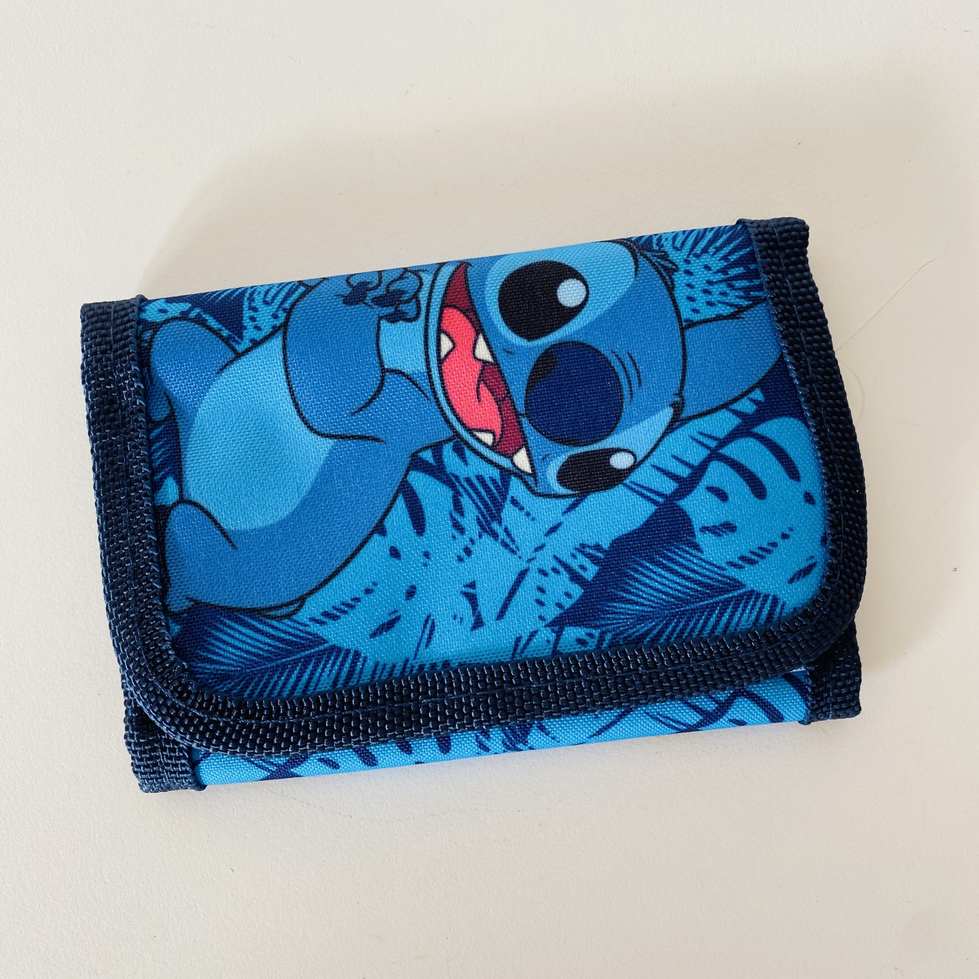Carteira azul com estampa do personagem Stitch e padrão de folhas.