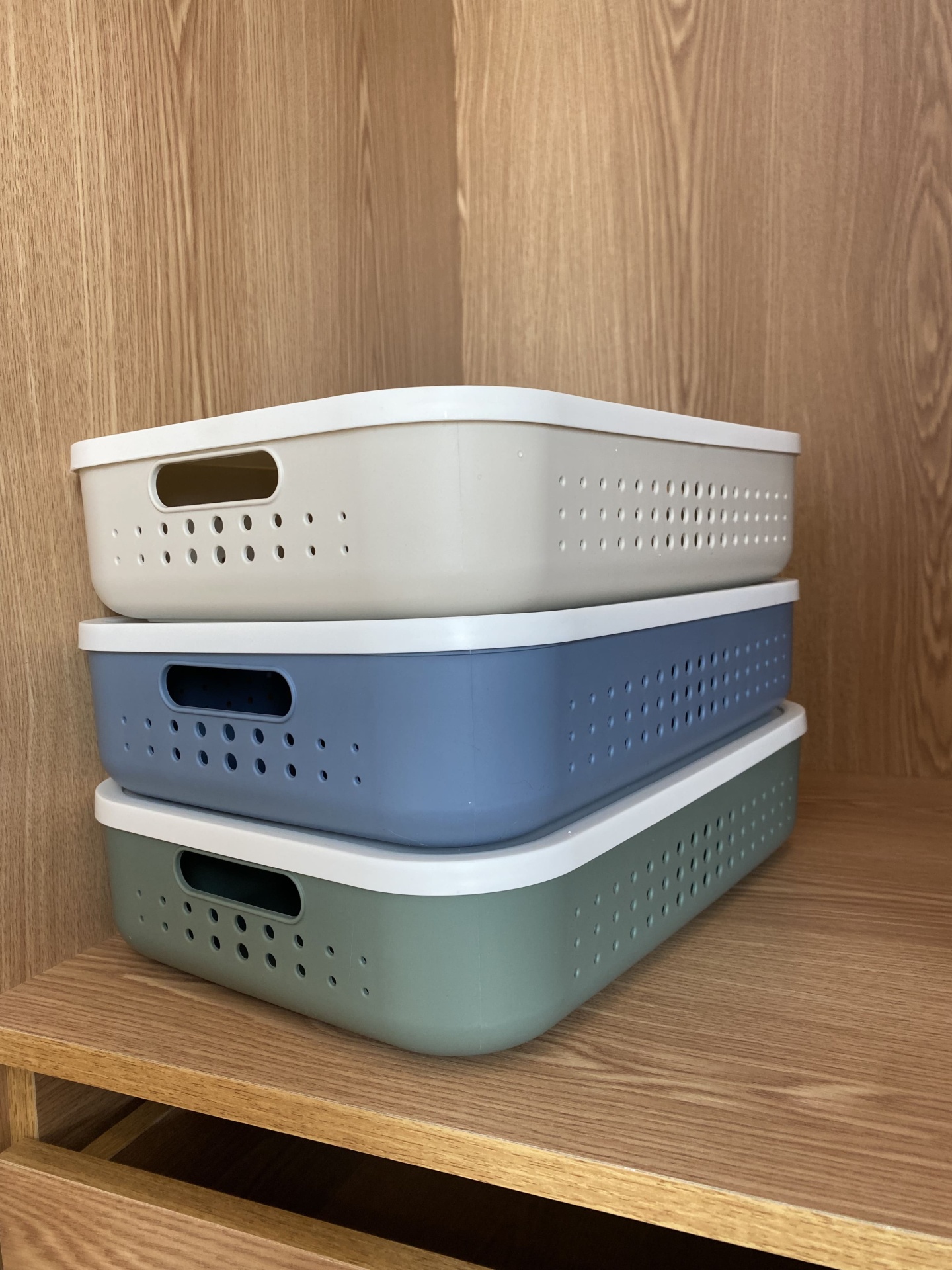 Três caixas organizadoras de plástico empilhadas em prateleira de madeira