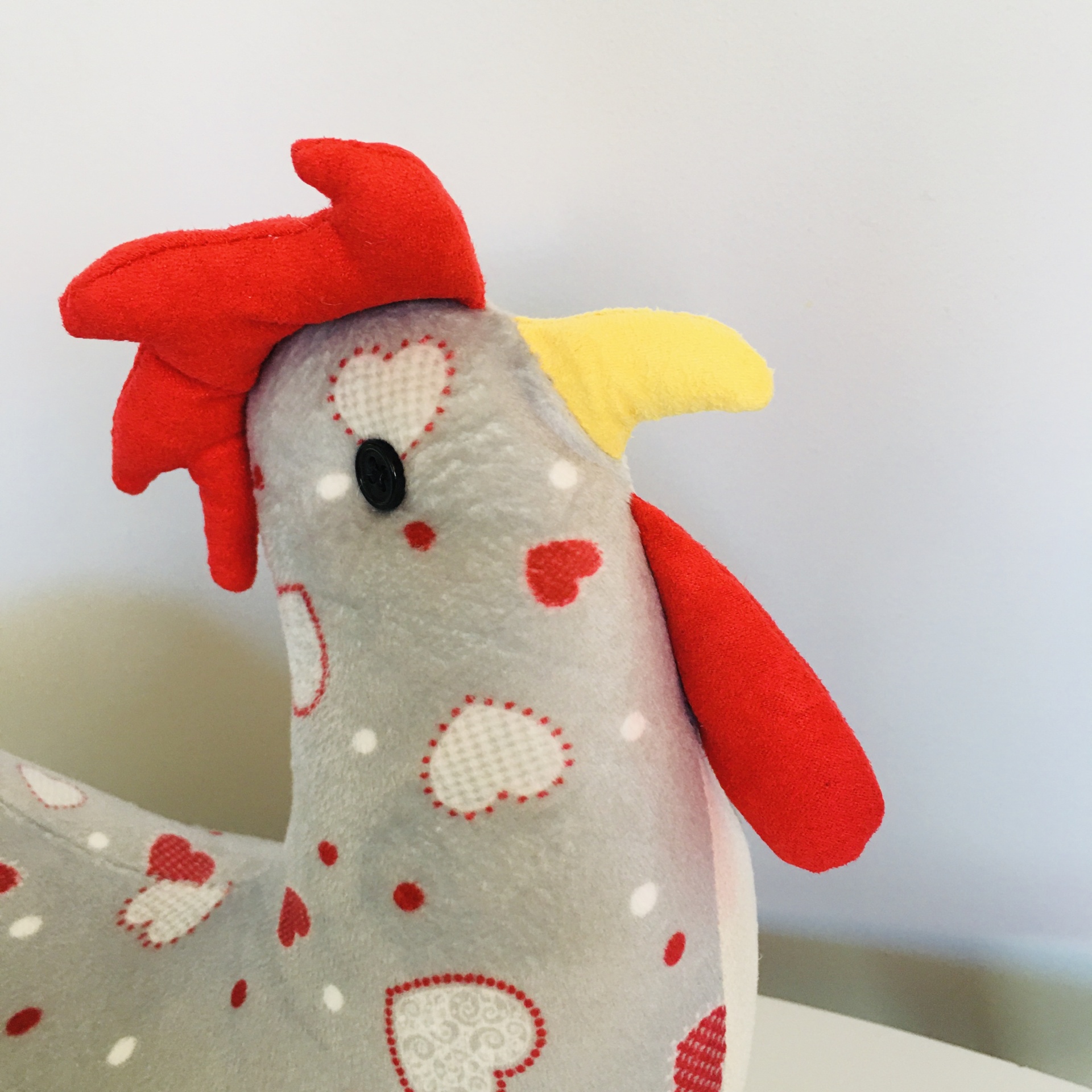 Pelúcia de galinha cinzenta com corações vermelhos e brancos, crista vermelha e bico amarelo