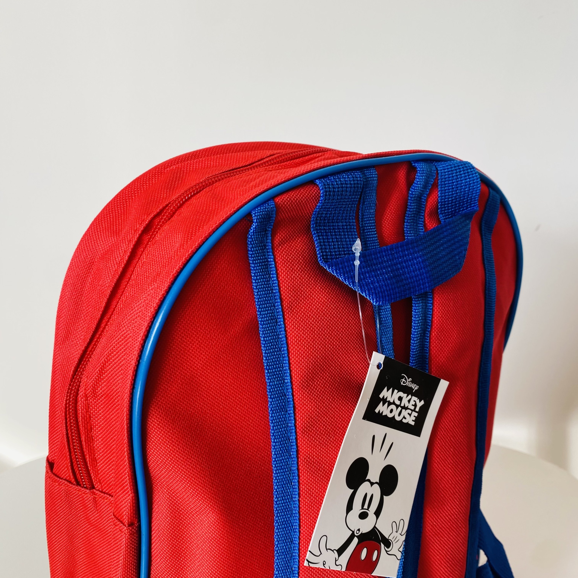 Mochila vermelha com detalhes azuis e etiqueta de Mickey Mouse