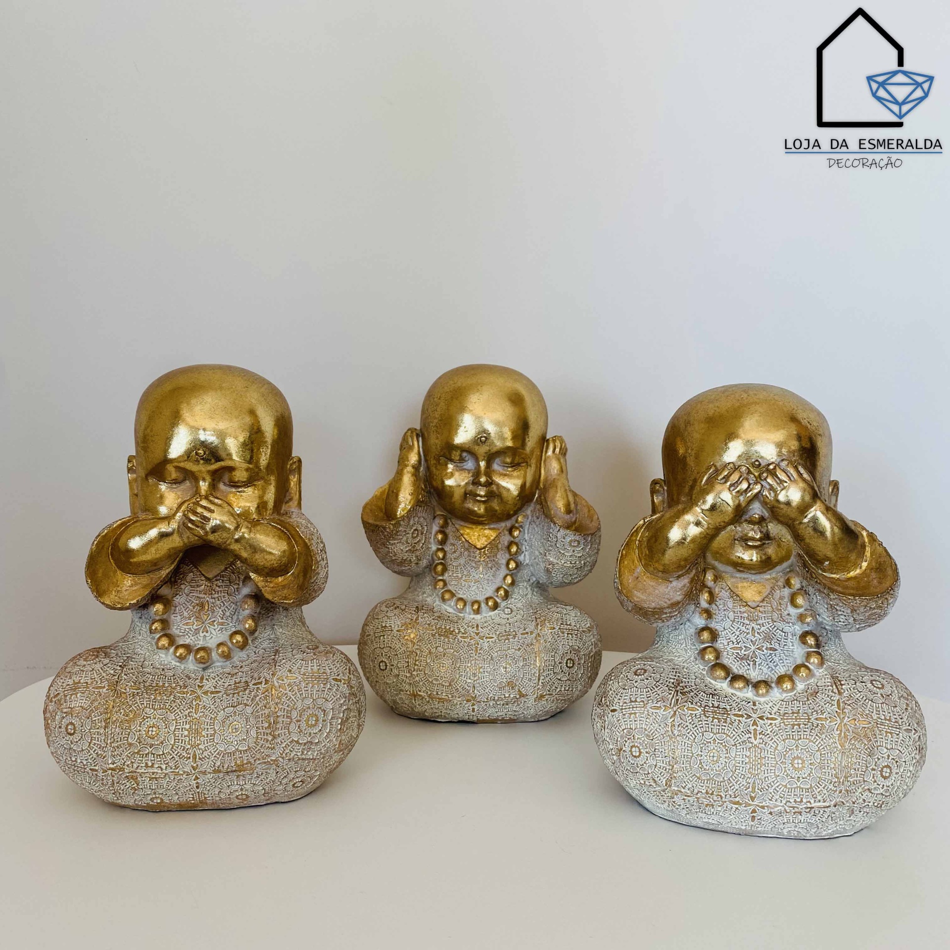 Três estatuetas decorativas em dourado e cinza de figuras budistas sentadas com colares dourados