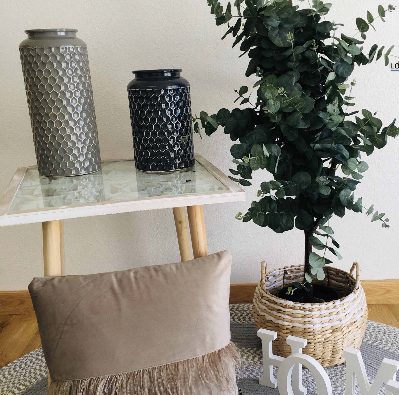 Vasos cerâmicos decorativos sobre mesa de mármore com planta em cesto de vime e almofada castanha