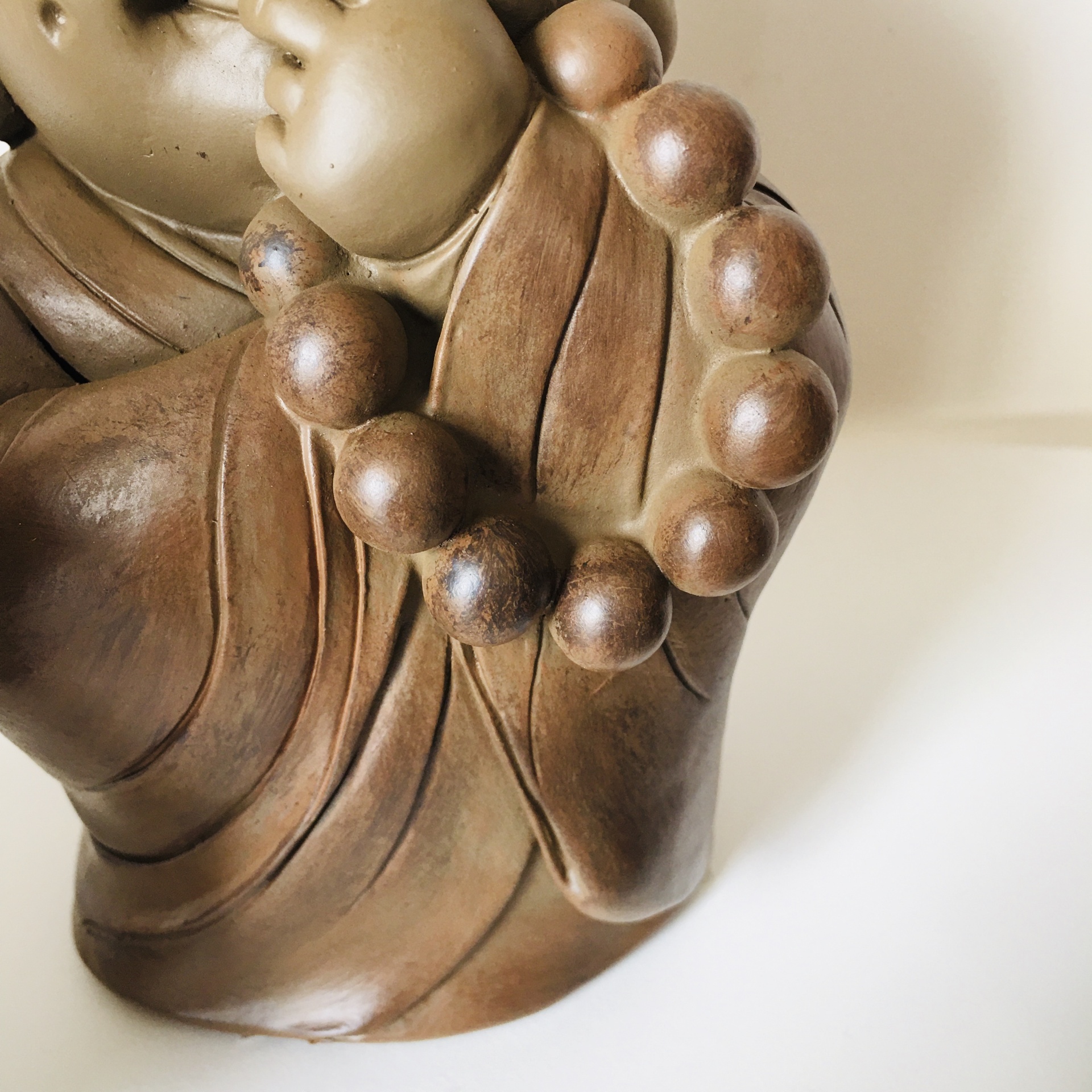 Escultura decorativa castanha com colar de contas grandes e fundo branco