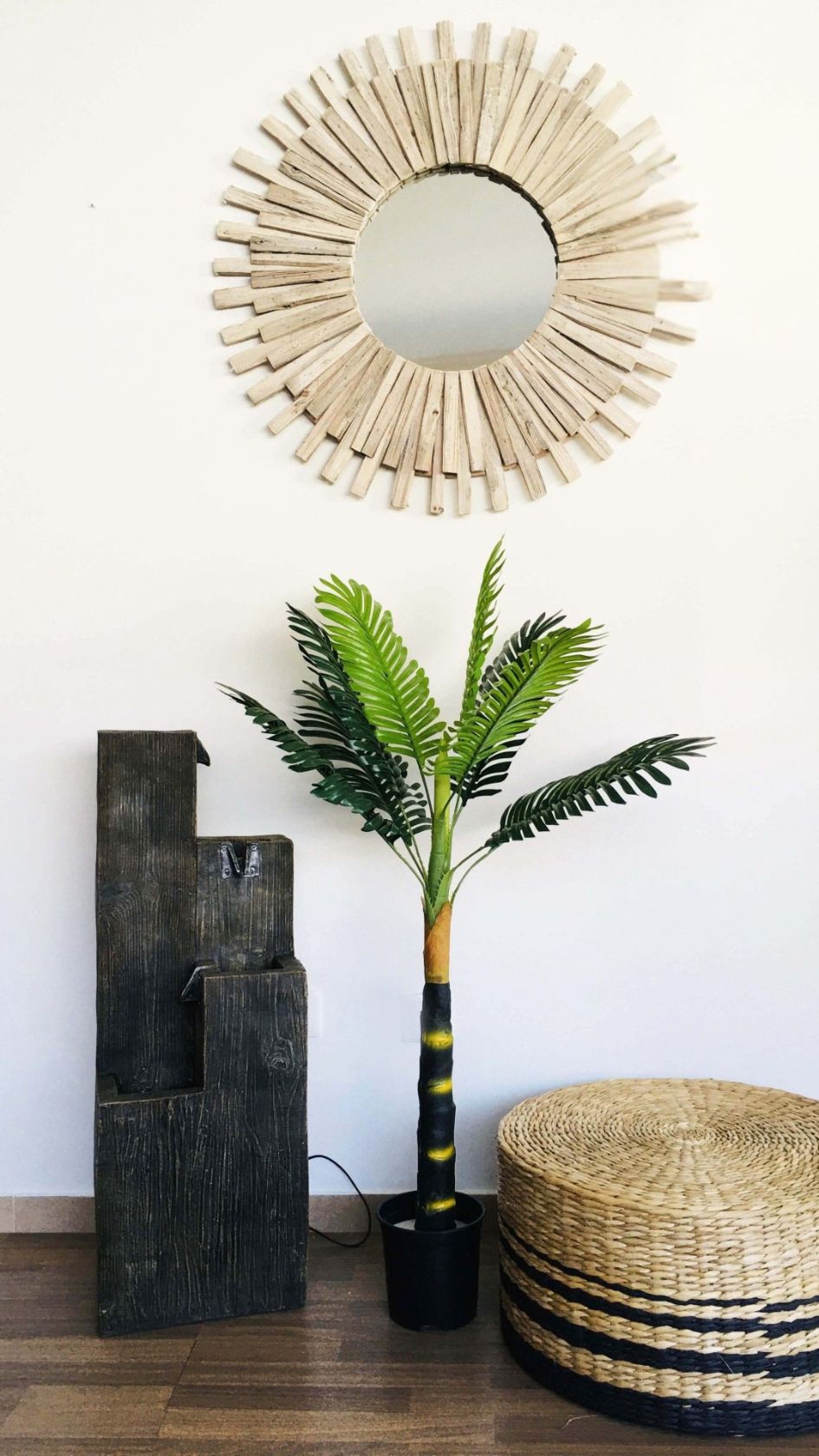 Espelho redondo de madeira com planta artificial, escultura preta e pufe de palha