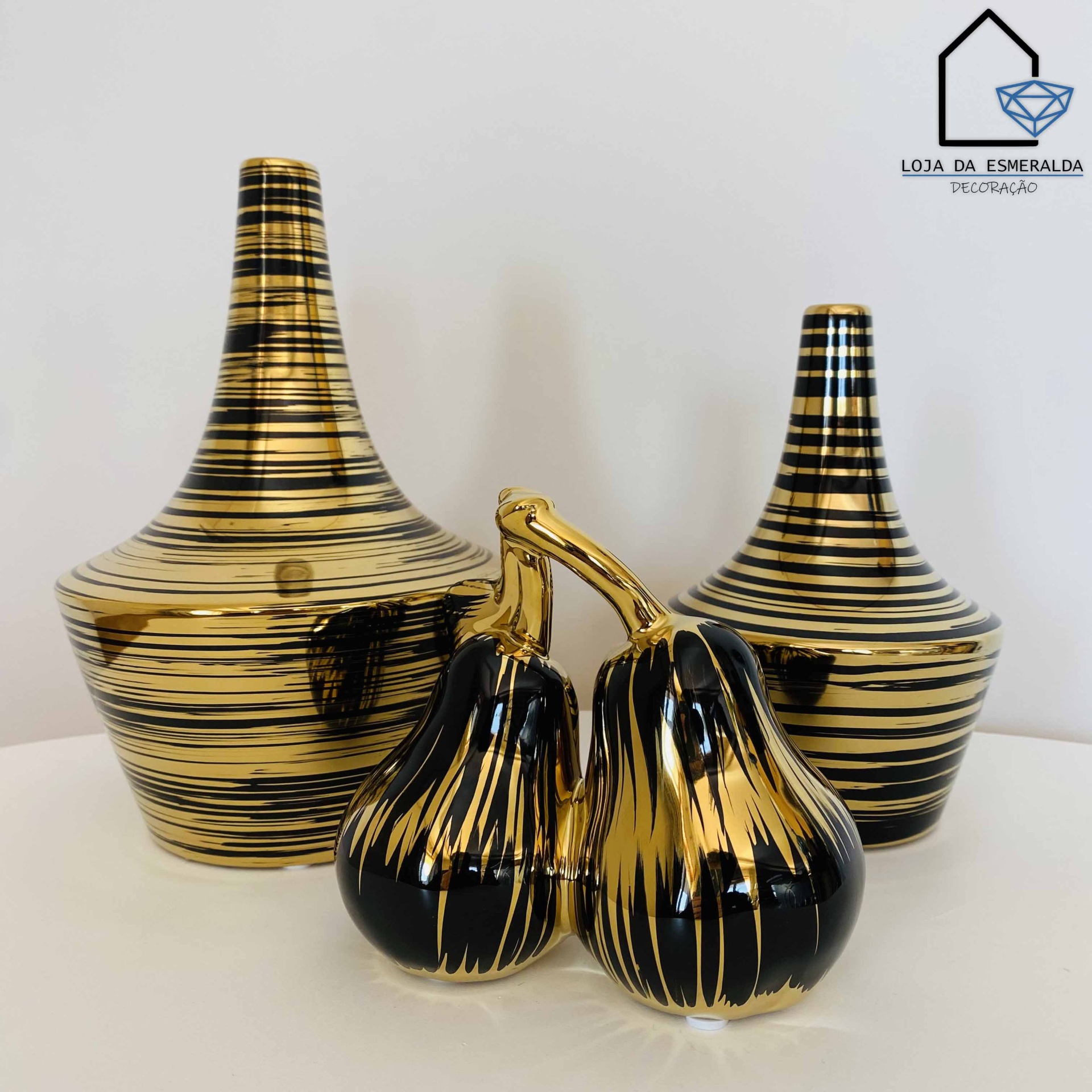 Conjunto de cerâmica com duas garrafas listradas em preto e dourado e duas cenouras douradas e pretas sobre superfície branca