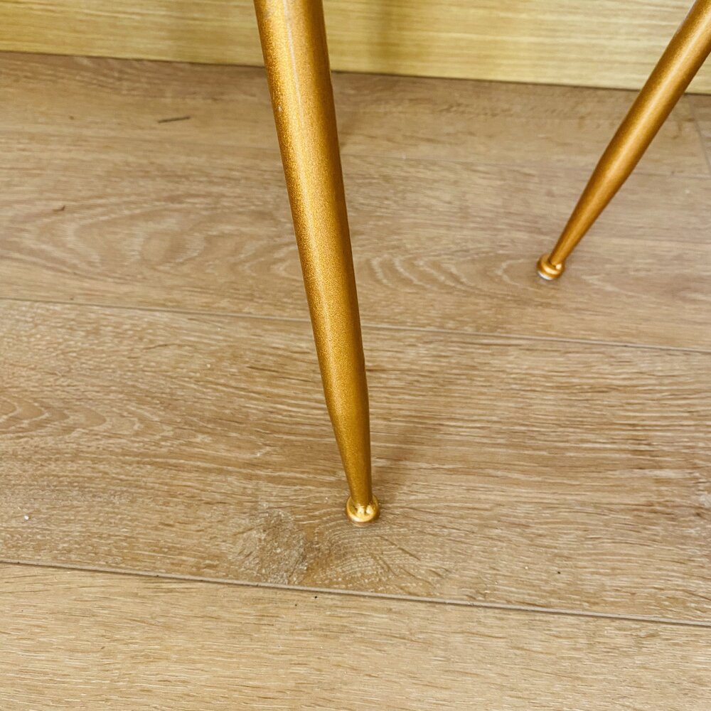 Pé metálico dourado sobre chão de madeira clara