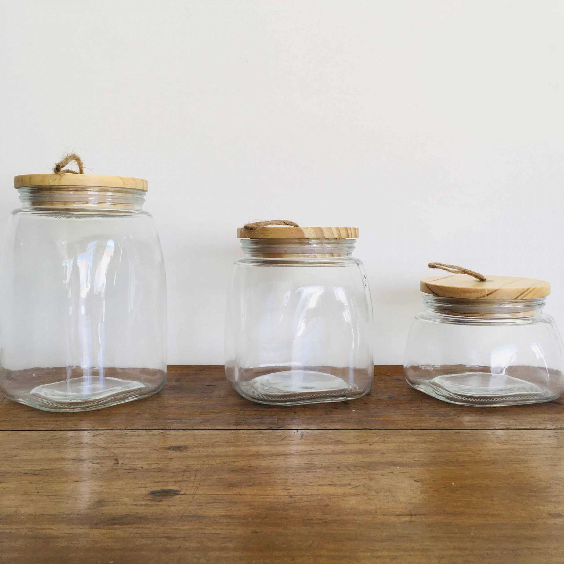 Três frascos de vidro com tampas de madeira numa mesa de madeira