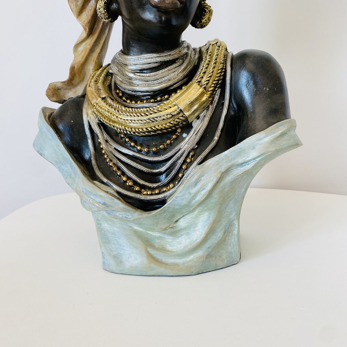 Busto decorativo de mulher com múltiplos colares dourados, vestido azul-pálido