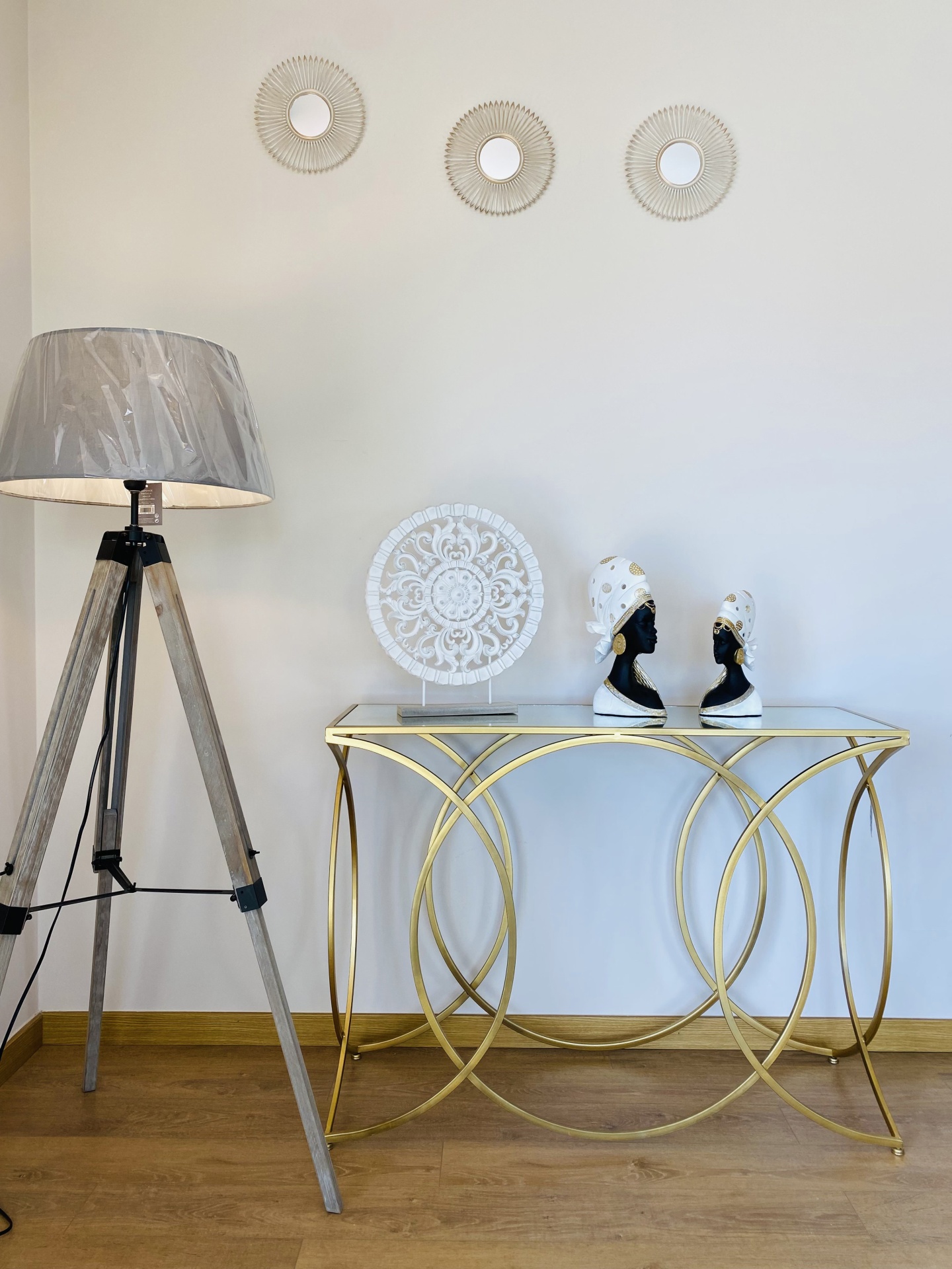 Conjunto decorativo com abajur, mesa dourada com tampo espelhado, três espelhos redondos na parede e peças decorativas sobre a mesa