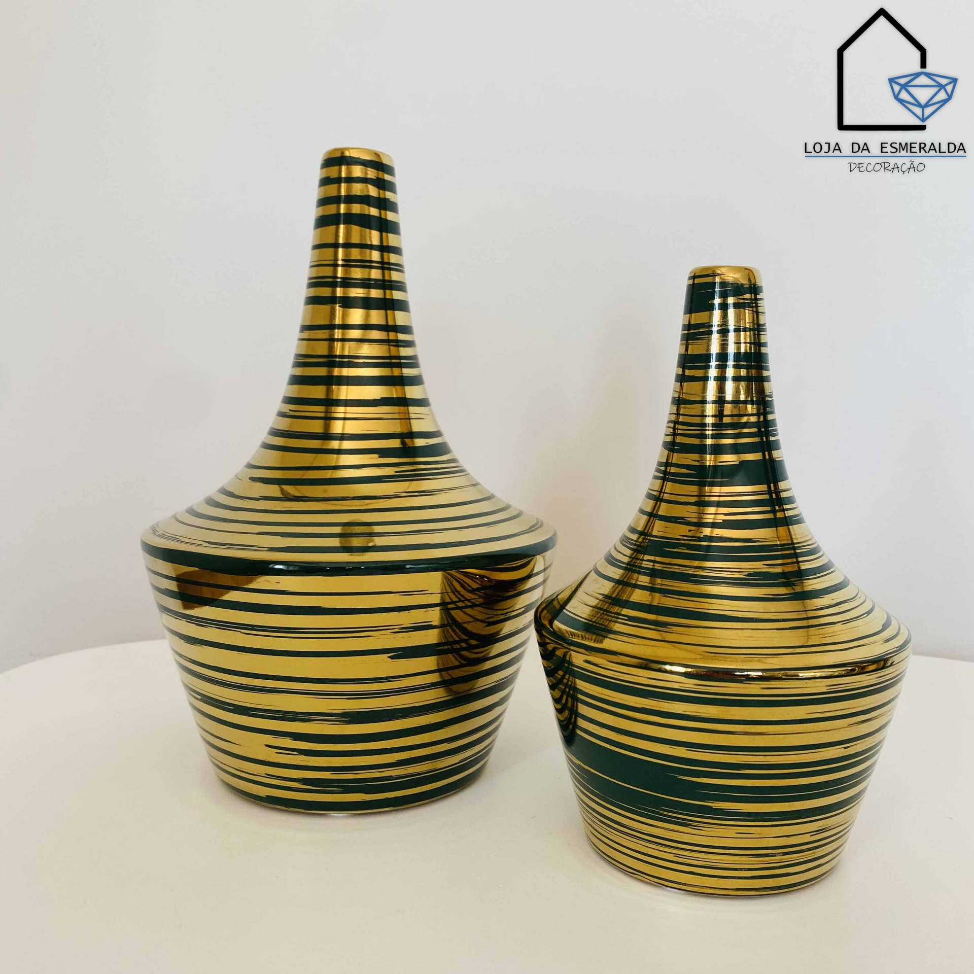 Dois vasos dourados com listras pretas em cerâmica, sobre uma superfície branca, ao lado do logótipo LOJA DA ESMERALDA DECORAÇÃO
