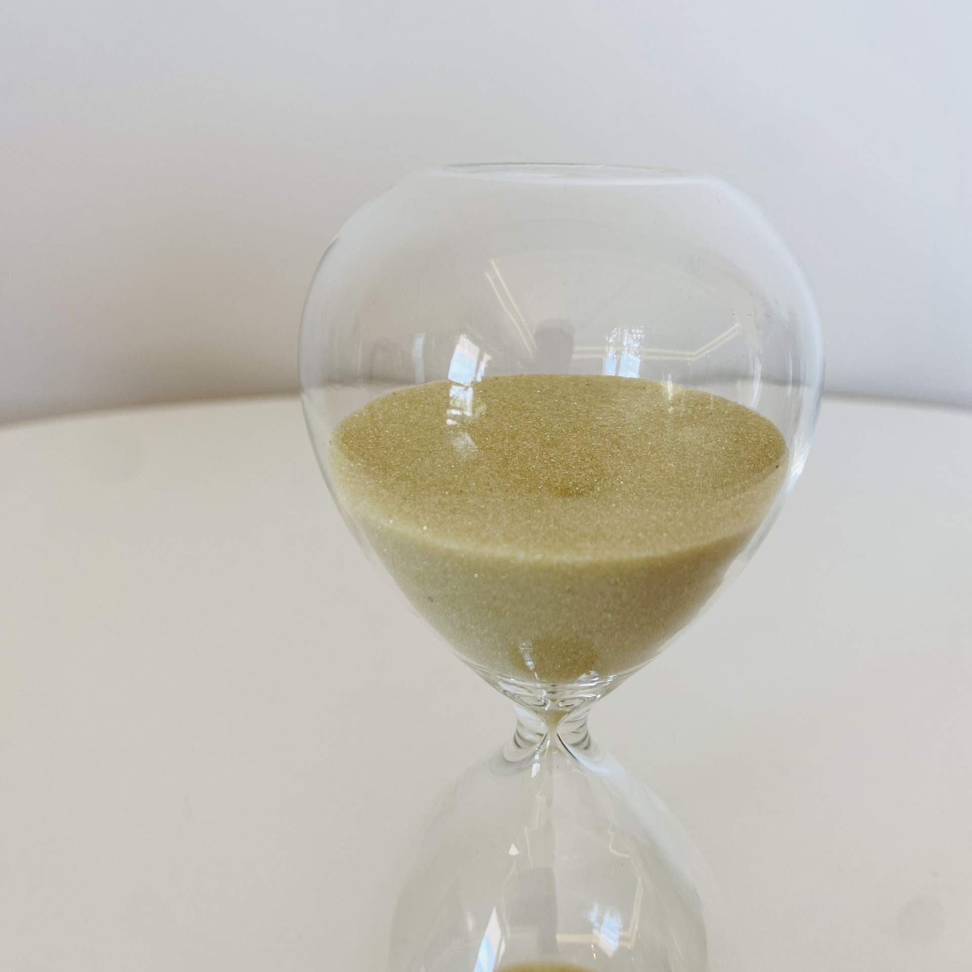 Ampulheta de vidro com areia amarela numa superfície branca