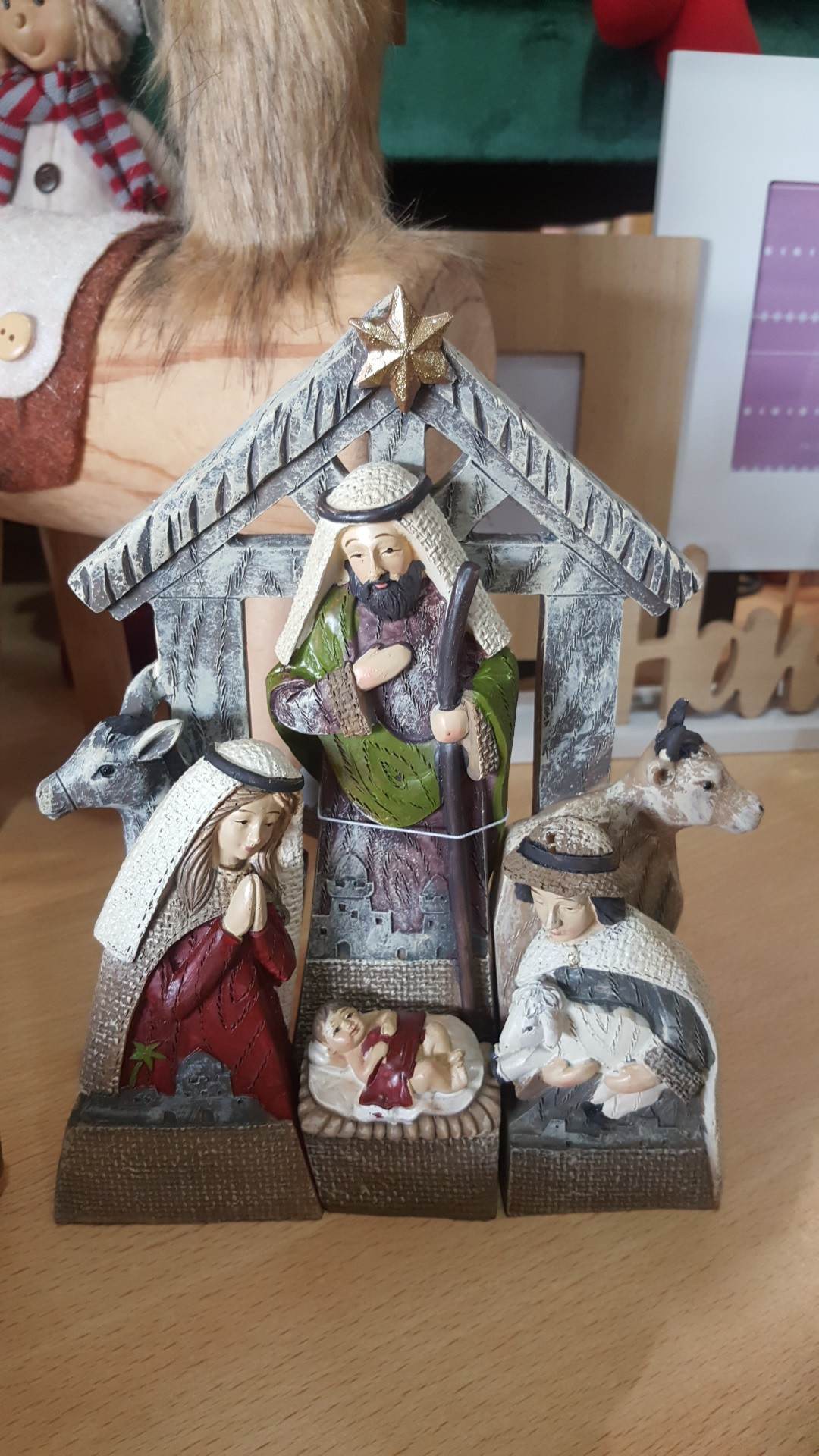 Presépio em resina com Maria, José, Menino Jesus, pastor e animais num estábulo cinzento com estrela dourada no topo