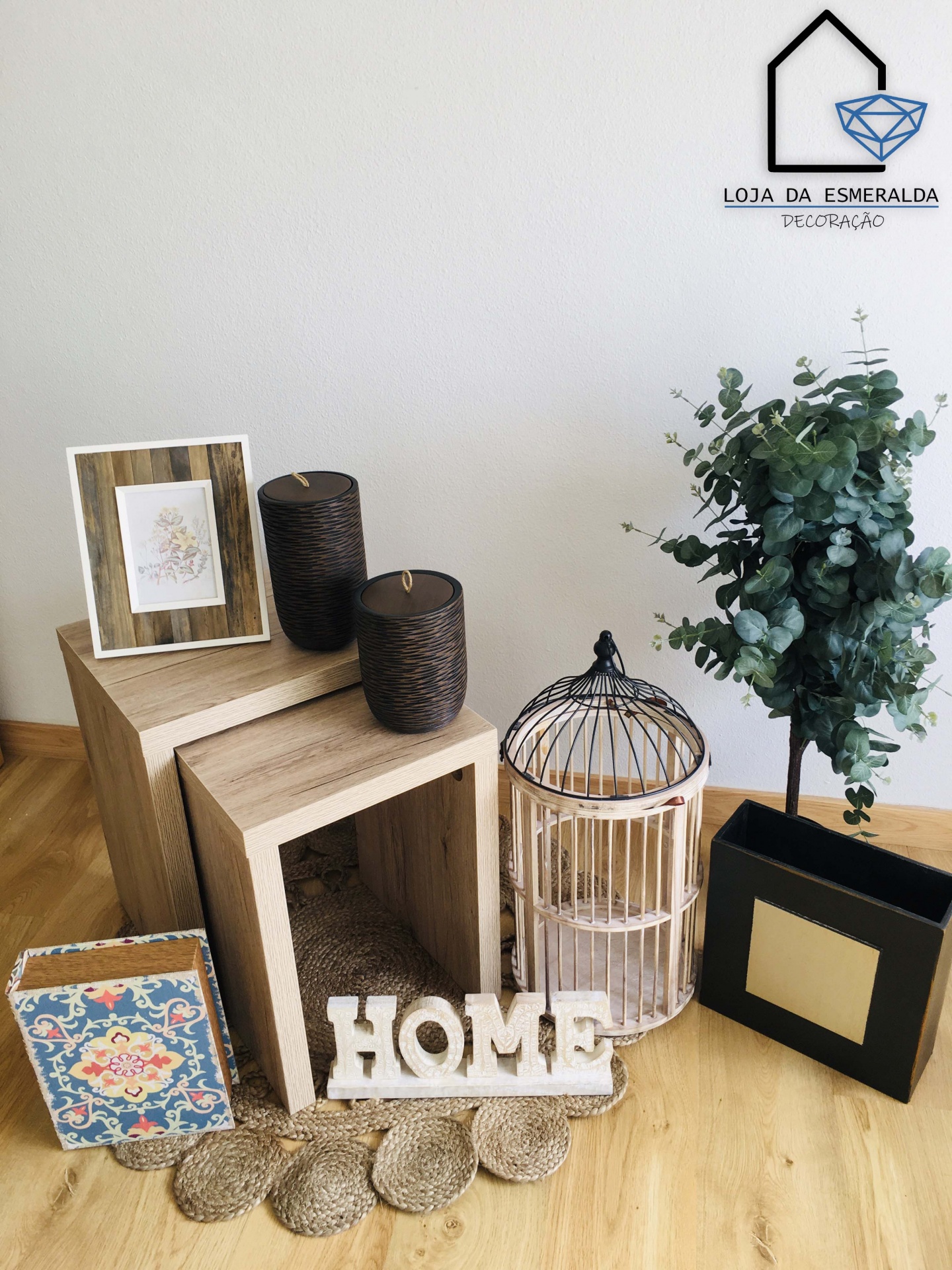 Conjunto decorativo com caixas de madeira, velas, gaiola decorativa e molduras em ambiente de chão de madeira clara