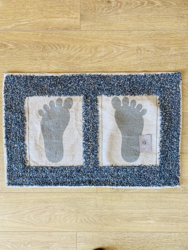 Tapete com pegadas cinzentas e borda azul sobre chão de madeira
