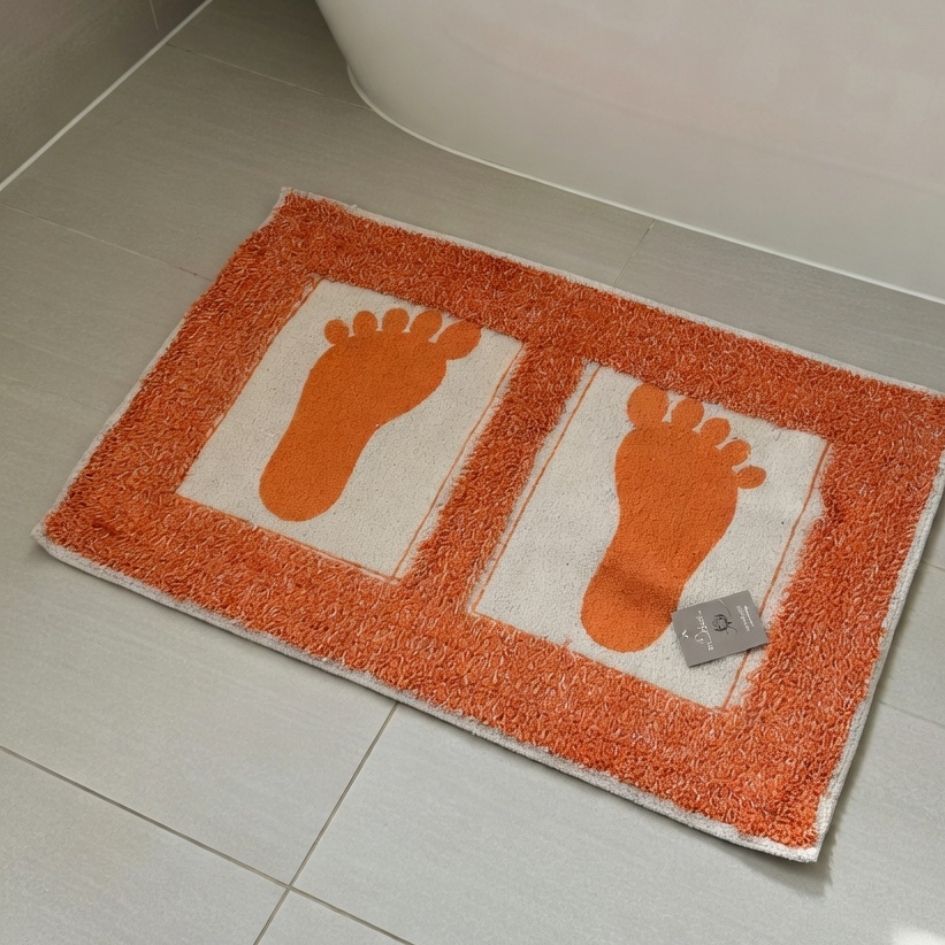 Tapete de banheiro branco e laranja com pegadas laranjas sobre chão de azulejos cinza