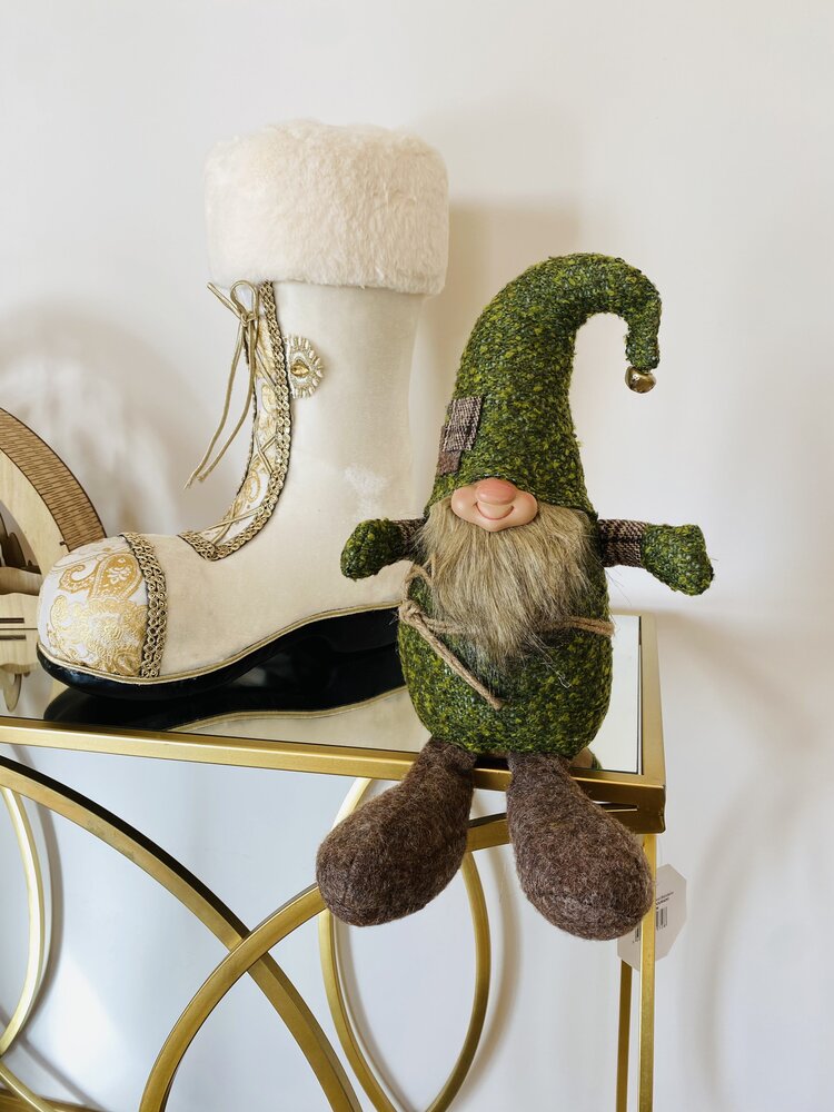 Bota decorativa branca com pelúcia e gnomo decorativo verde sentados numa mesa dourada com tampo de vidro