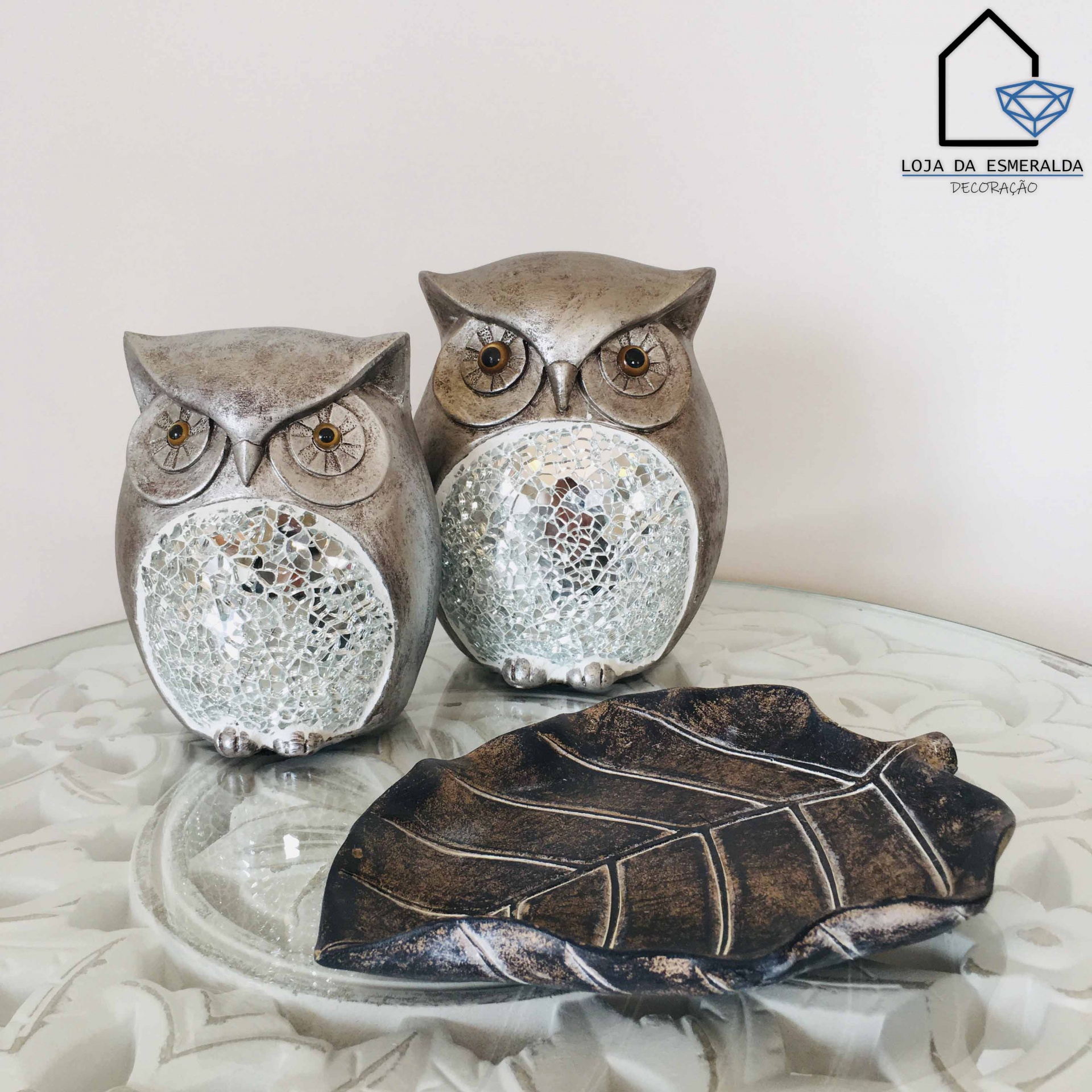 Conjunto decorativo com duas corujas metálicas e prato em forma de folha sobre mesa de vidro
