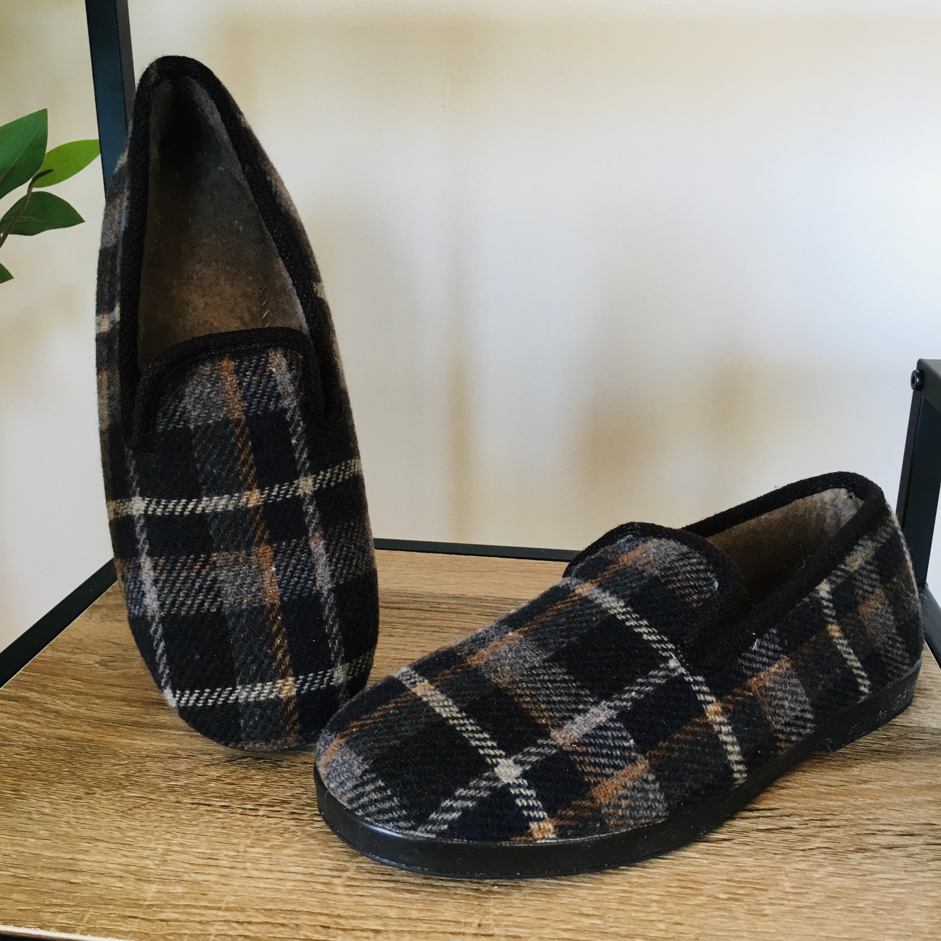 Chinelos tipo mocassim xadrez castanho e preto sobre madeira clara