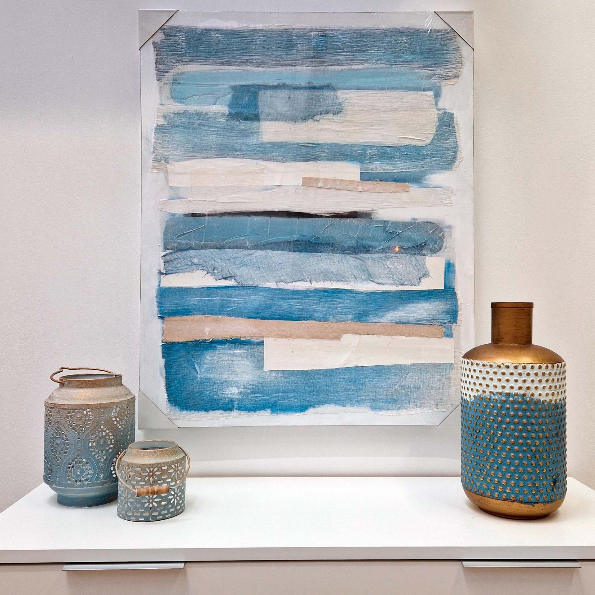 Quadro abstrato azul e branco com três objectos decorativos azuis e castanhos sobre superfície branca