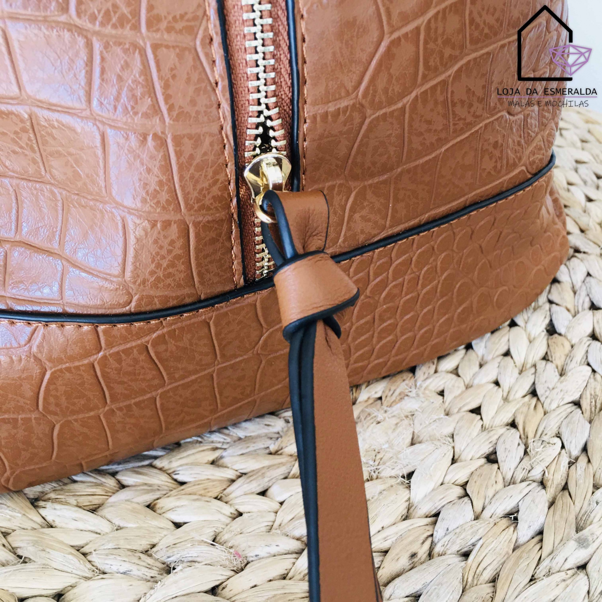 Mala castanha com padrão pele de crocodilo e fecho dourado sobre superfície trançada