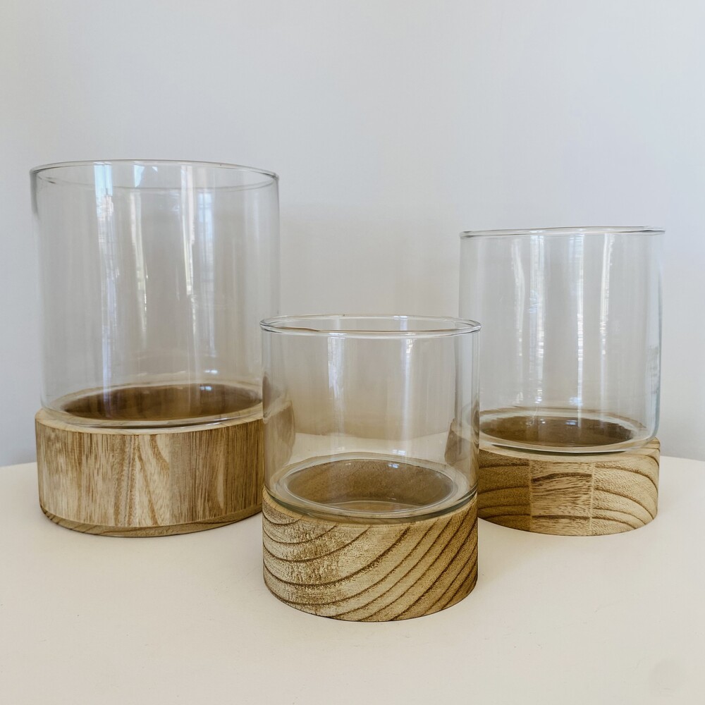 Três copos de vidro com bases de madeira em diferentes tamanhos num fundo branco