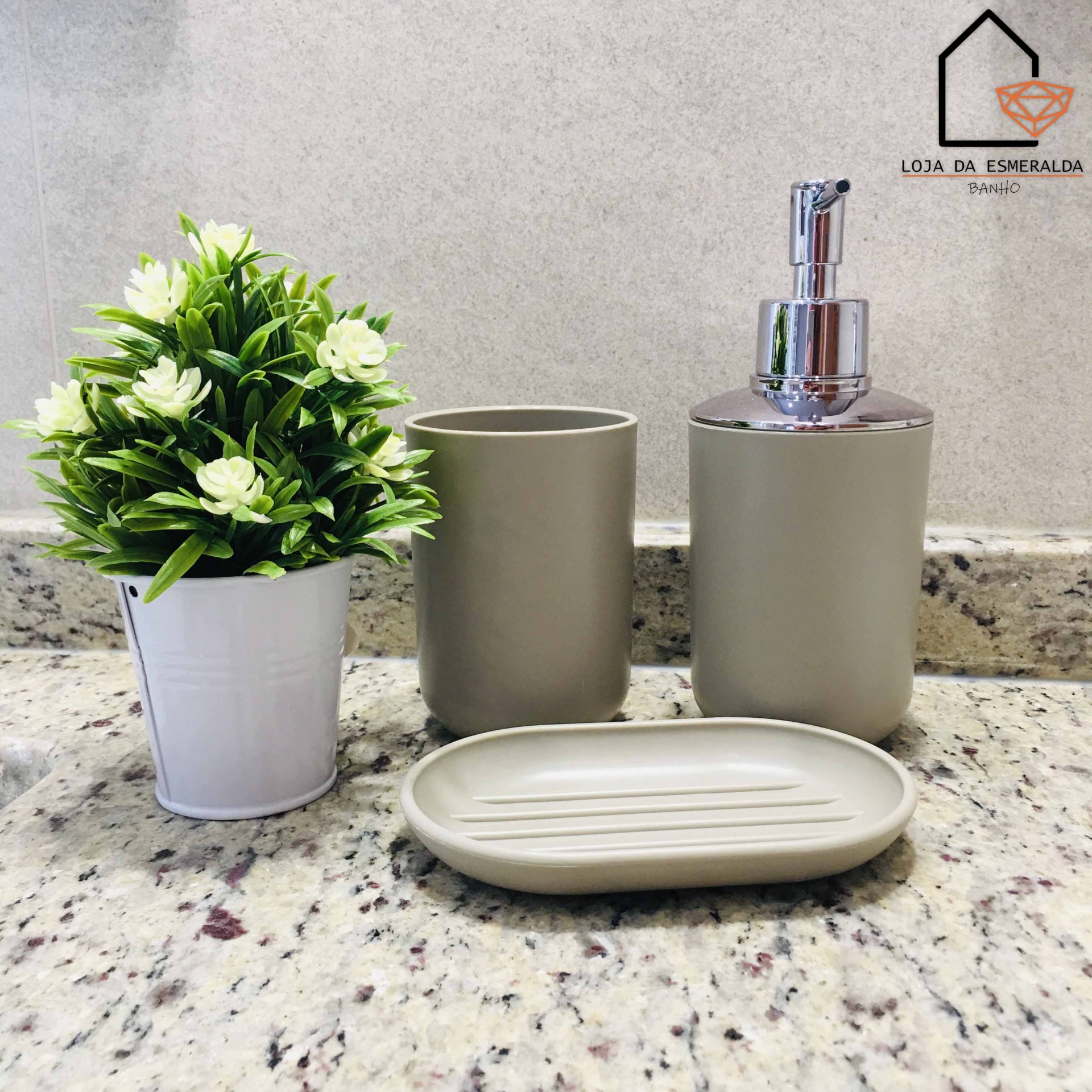 Conjunto de acessórios de casa de banho cinzentos junto a planta artificial em vaso branco
