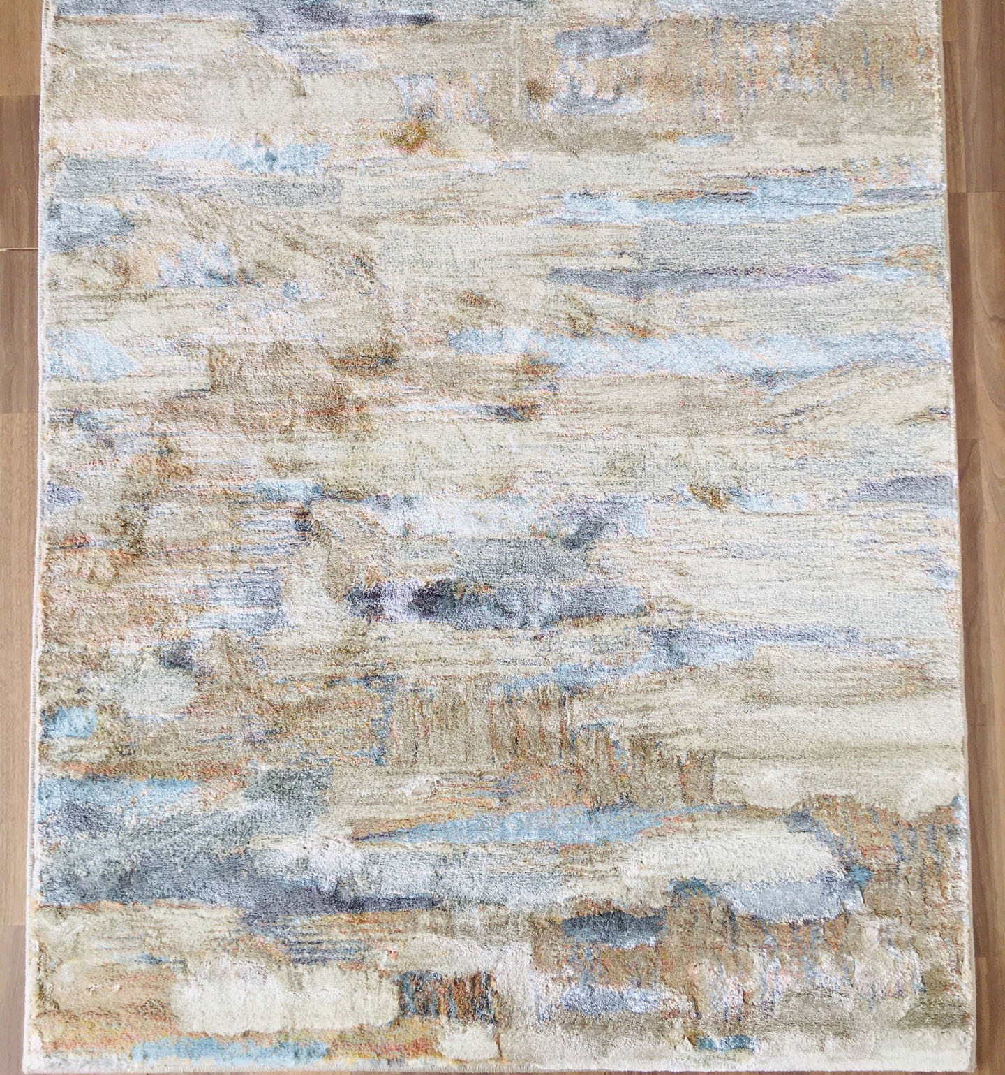 Tapete retangular abstrato bege azul cinza castanho com textura aveludada em chão de madeira