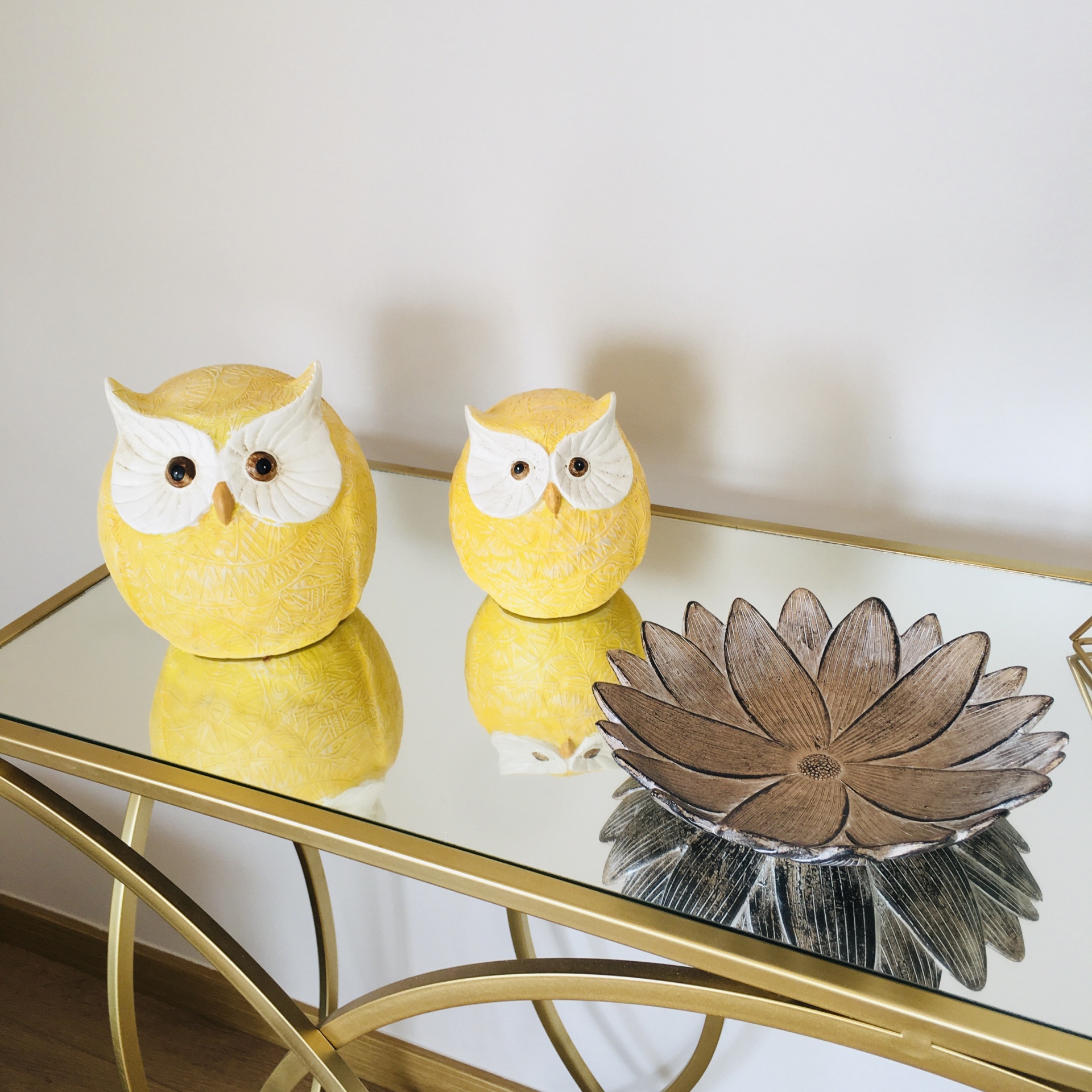 Conjunto decorativo com duas corujas amarelas e uma peça metálica em flor sobre mesa espelhada dourada
