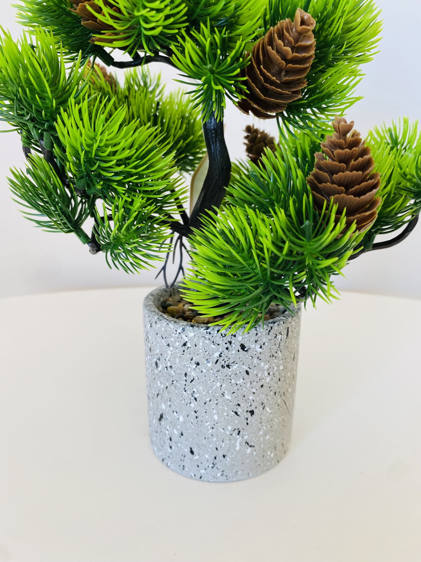 Vaso cinza com planta artificial verde e pinhas castanhas.