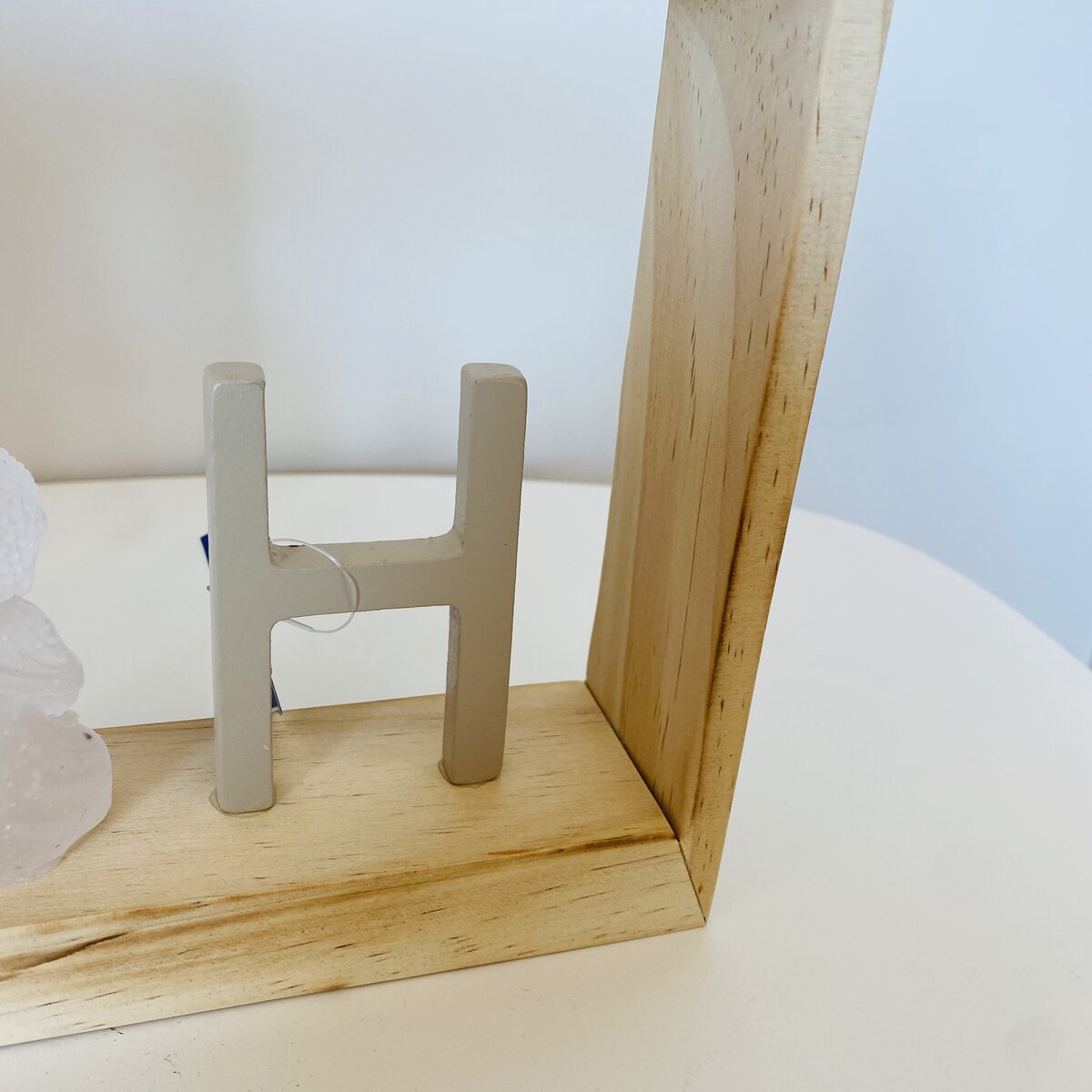 Letra decorativa H cinzenta numa base de madeira clara sobre superfície branca