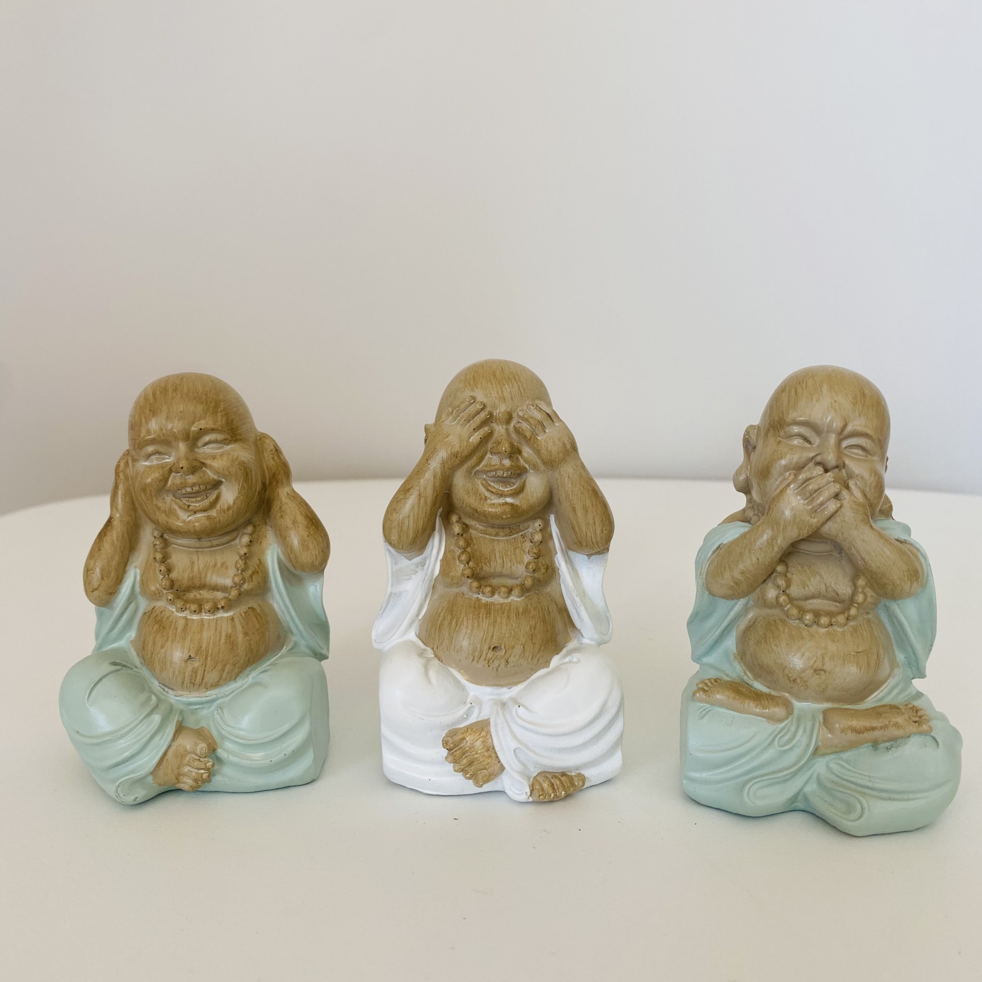 Três estatuetas decorativas de Buda sentado em azul claro e branco.