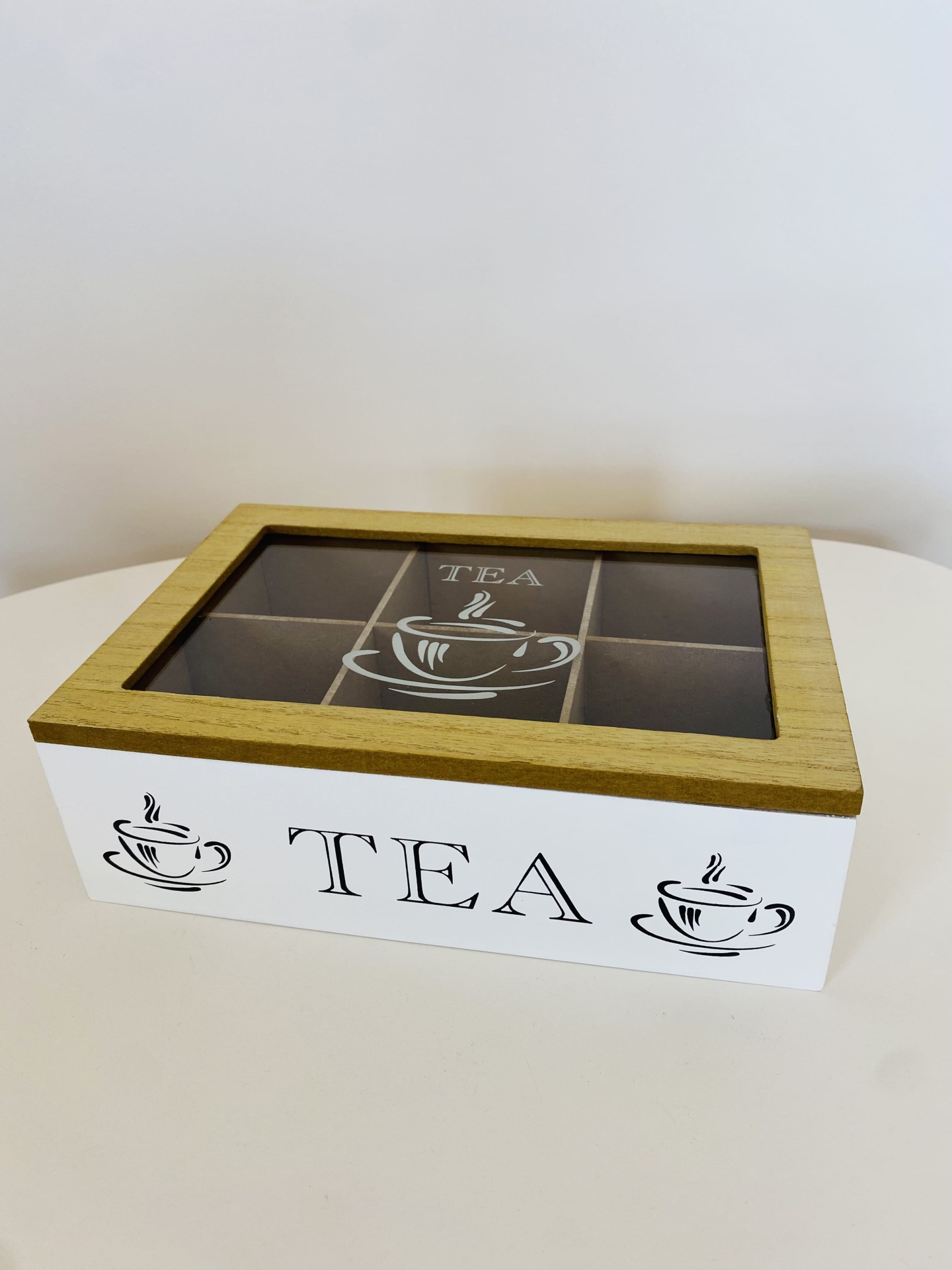 Caixa de chá branca com tampa em madeira clara e visor de vidro, decorada com chávenas e texto TEA